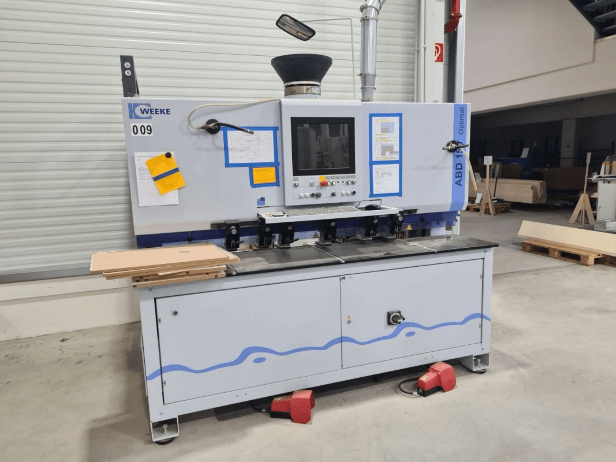 HOMAG WEEKE OPTIMAT ABD150 máquina de perfuração multi-fuso, vista frontal, mostrando os controlos e painéis de madeira empilhados.