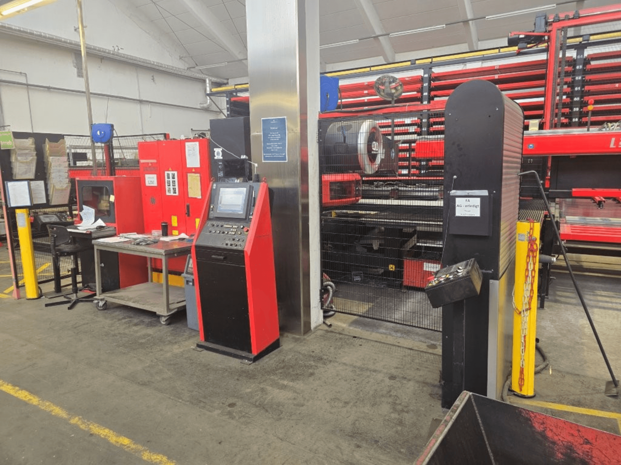 Vista frontal da máquina de perfuração CNC AMADA EMZ 3610 NT, apresentando os comandos do operador e a cabina de segurança num ambiente fabril.