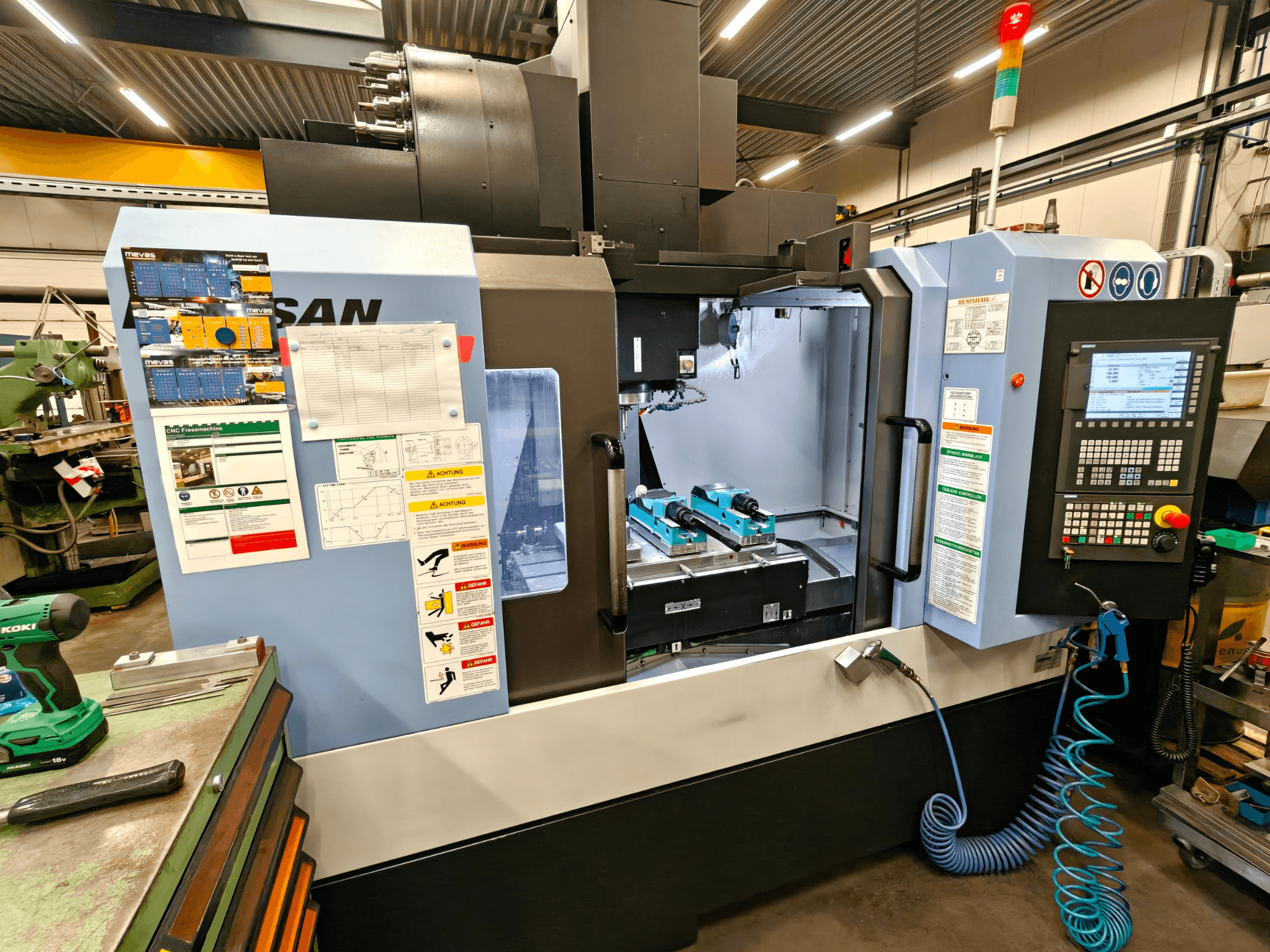 Centro de maquinação vertical DOOSAN DNM 400 II numa oficina, com controlos, suportes de ferramentas e sinalização de segurança, vista frontal.