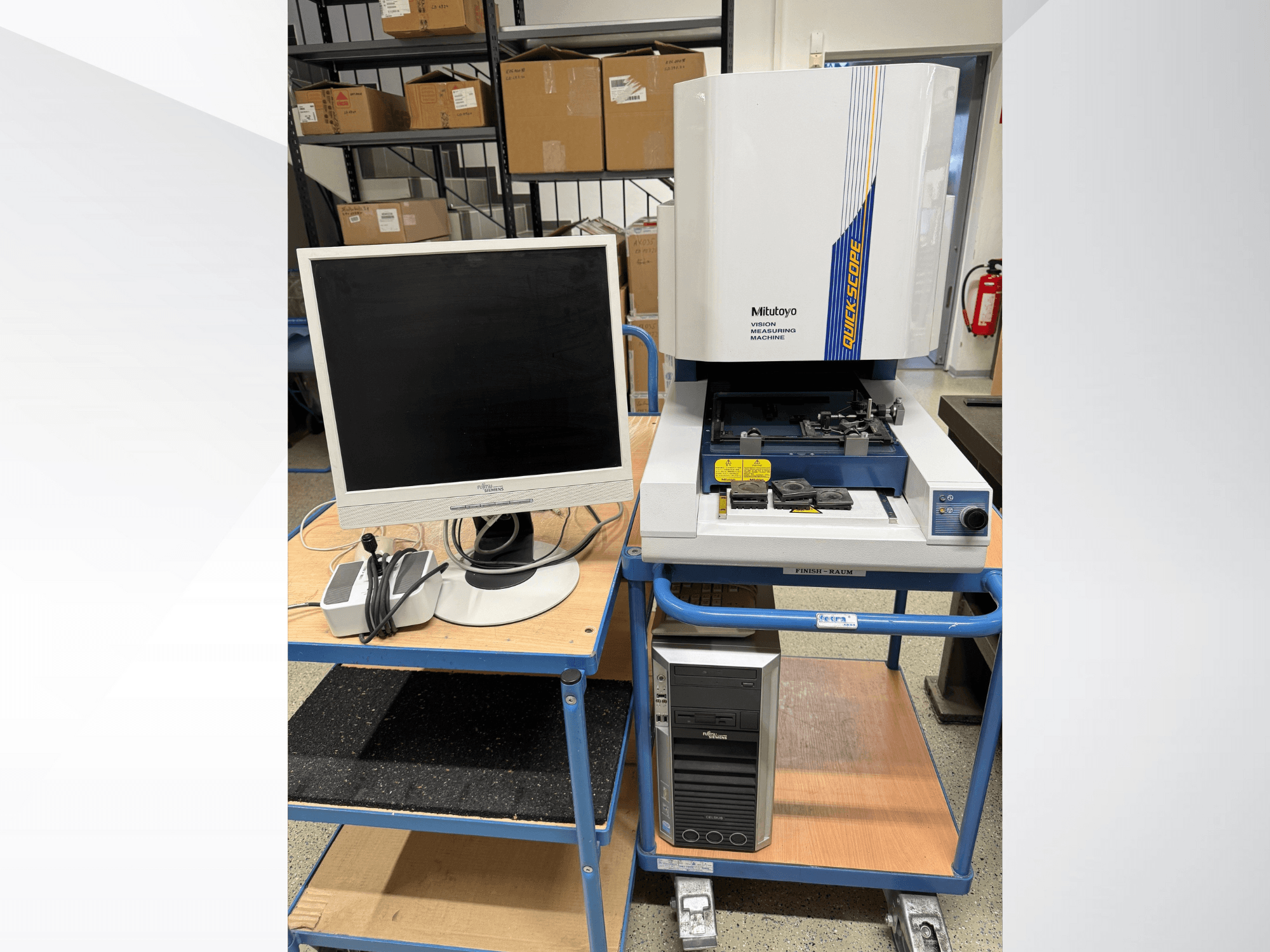 Máquina de medição visual Mitutoyo Quick Scope com monitor, PC e acessórios, vista frontal, num carrinho azul.