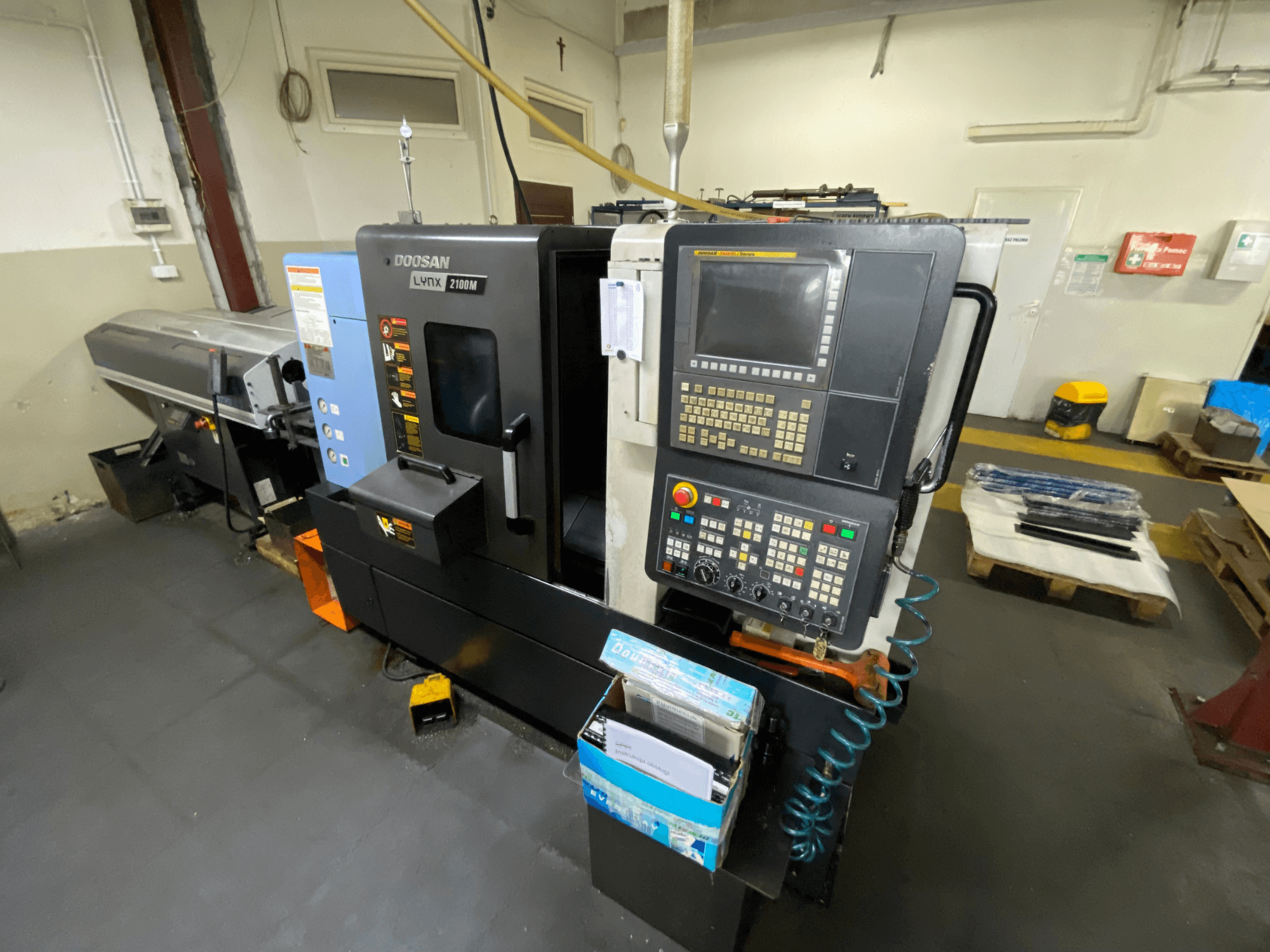 Torno horizontal DOOSAN LYNX 2100MA visto de perfil, apresentando o painel de controlo, as ferramentas e a área de trabalho.
