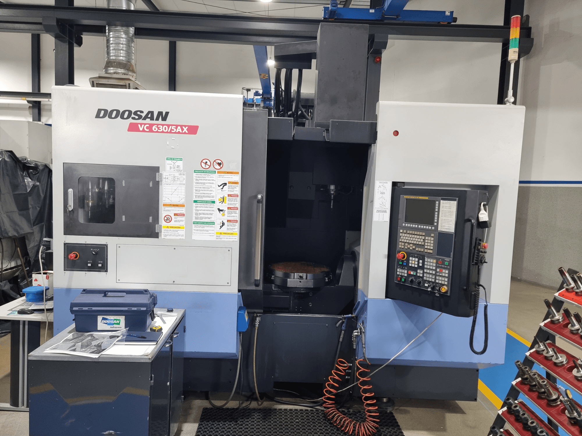 Centro de maquinagem universal DOOSAN VC 630/5AX, vista frontal que mostra o painel de controlo, a área de corte e os dispositivos de segurança.