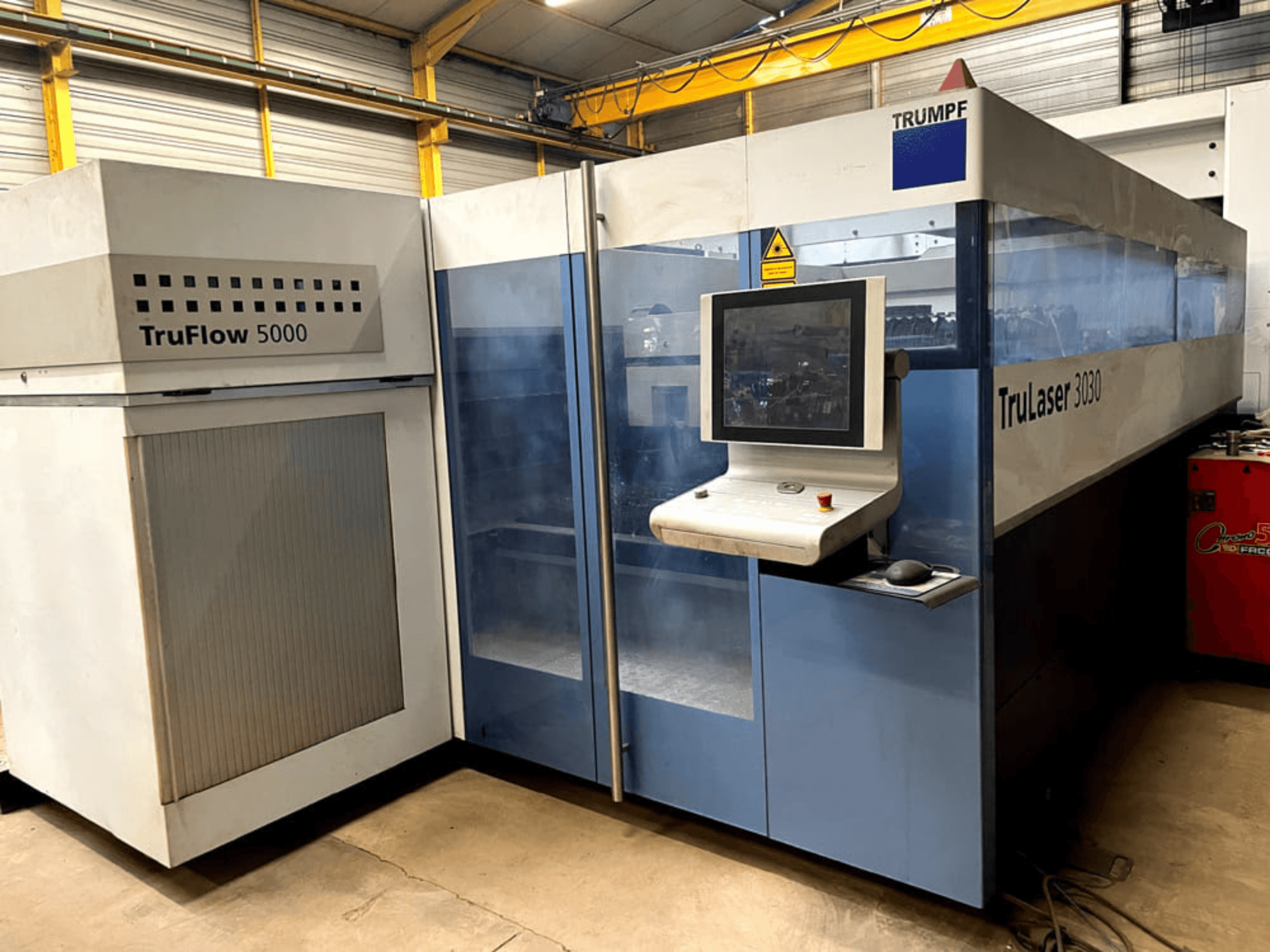 Máquina de corte a laser de CO₂ TRUMPF TruLaser 3030, vista de frente, com um painel de controlo e a unidade TruFlow 5000 adjacente.