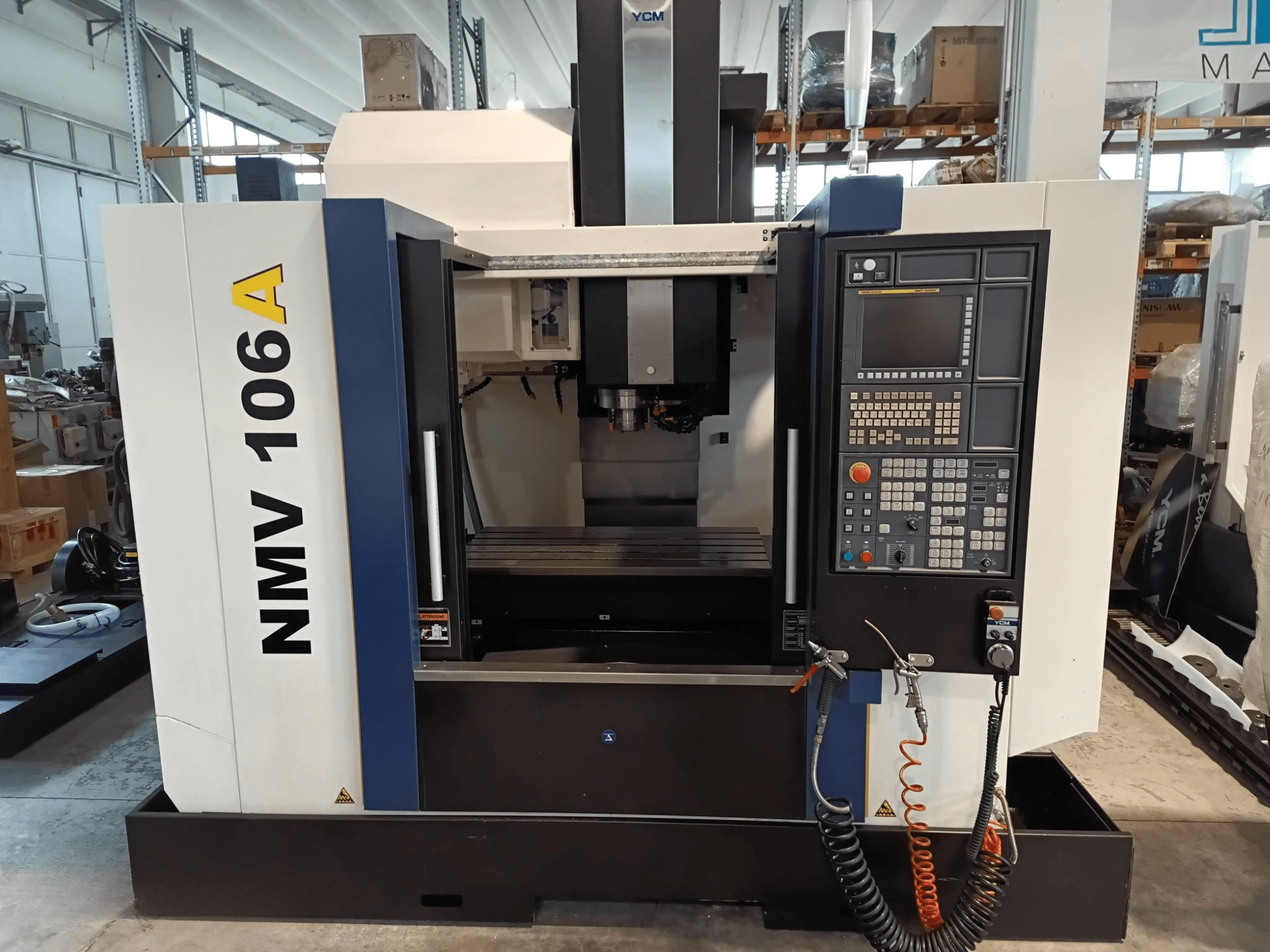 Centro de maquinação YCM NMV 106A, vista frontal, com painel de controlo com botões e mangueiras de refrigeração.