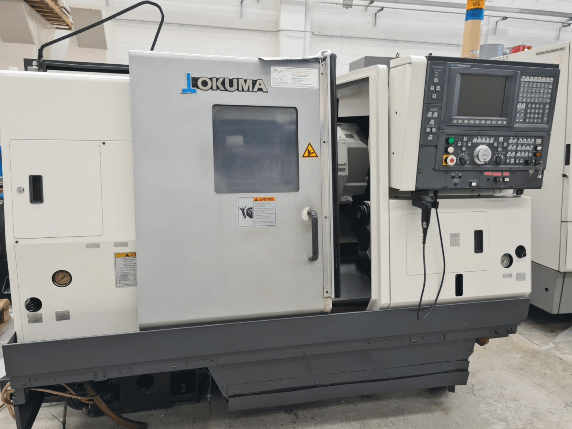 Okuma LB 300M X 500 máquina de torneamento horizontal em vista lateral, mostrando o painel de controlo, acesso ao fuso e avisos de segurança.