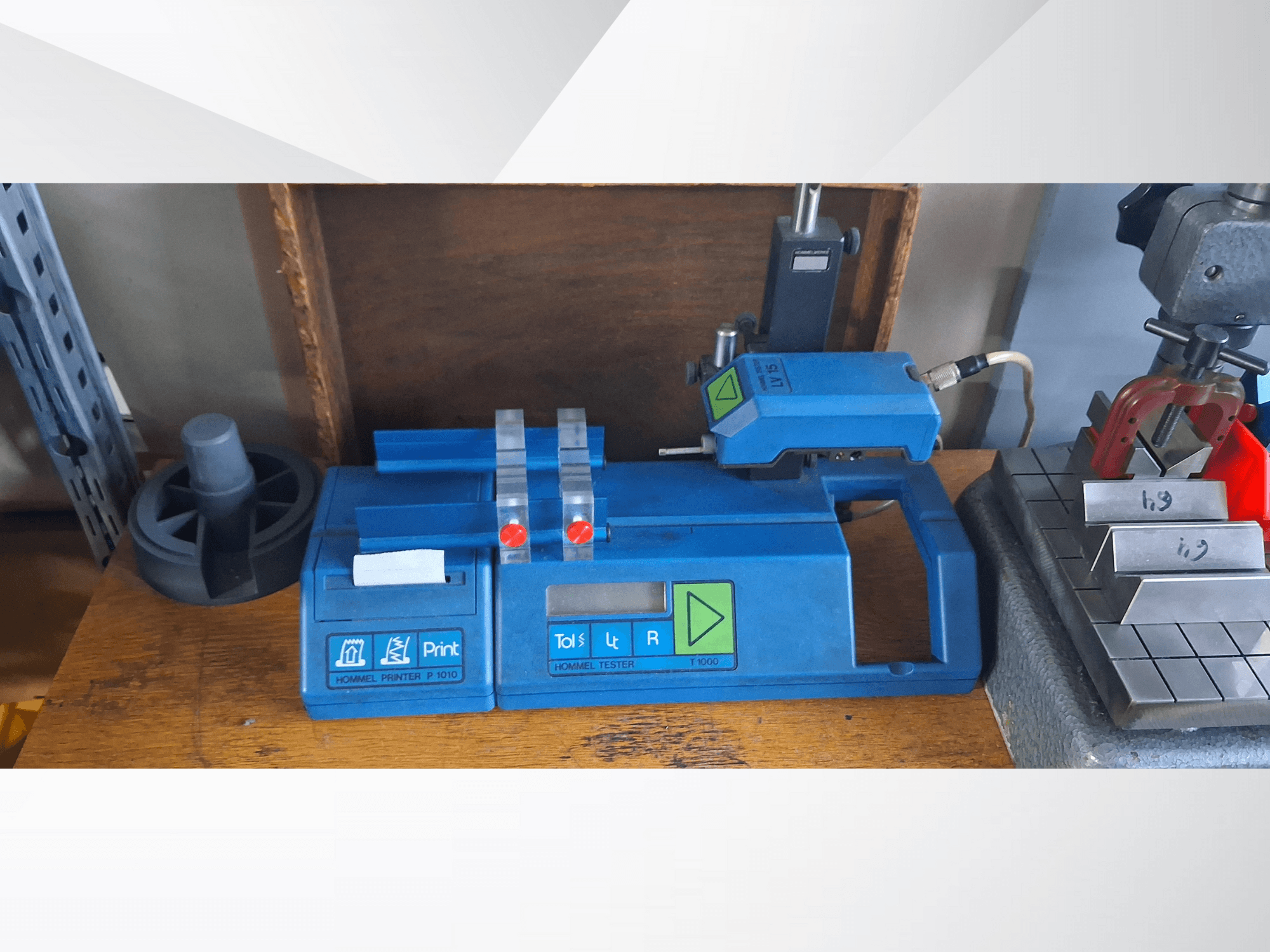 Impressora Hommel P 1010 e Tester T1000 em vista lateral, com caixa azul, botões e indicadores vermelhos, numa bancada de trabalho.