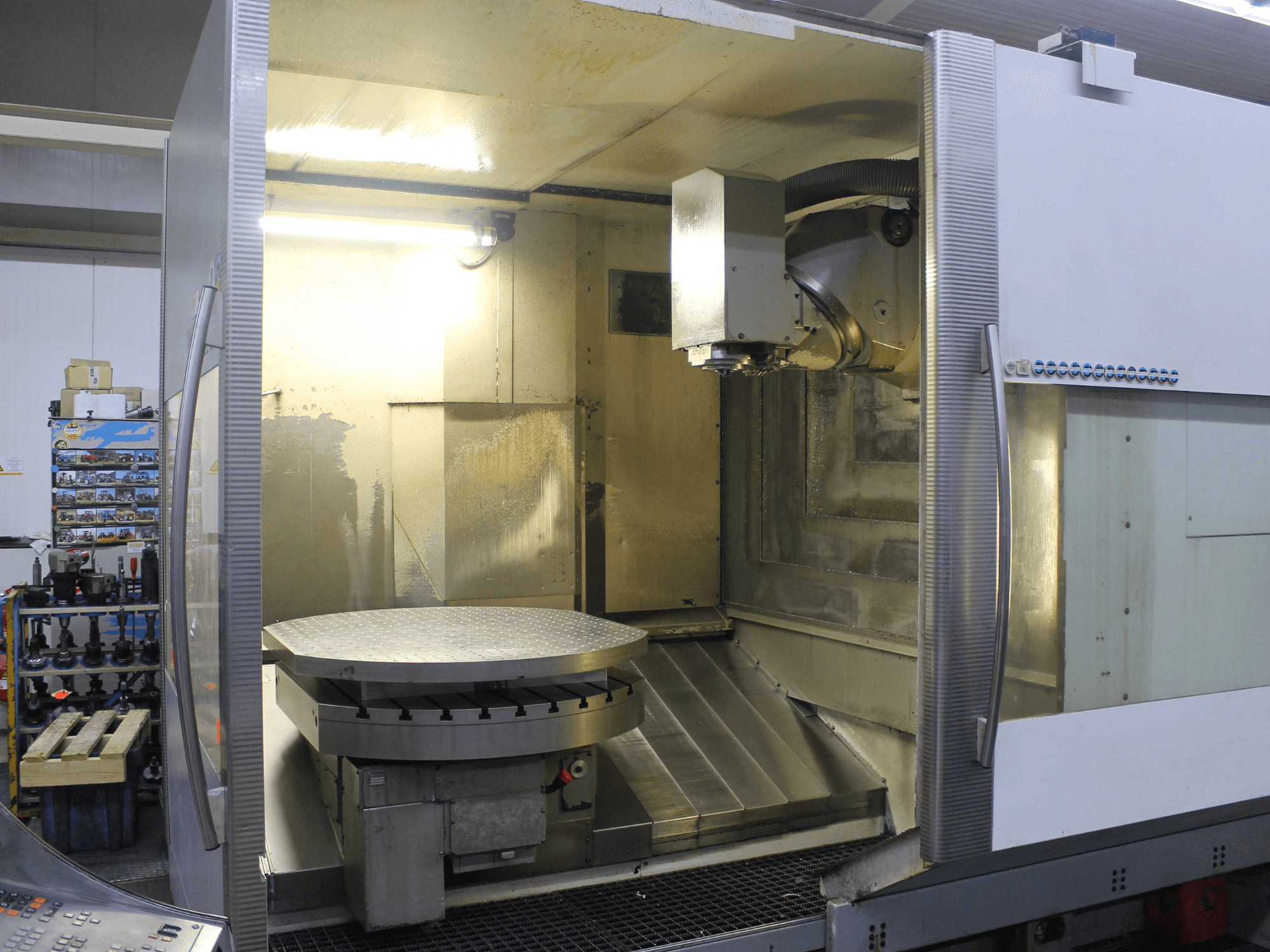 Fresadora CNC com mesa rotativa circular e cabeça de corte, vista de frente, com superfícies metálicas e iluminação.