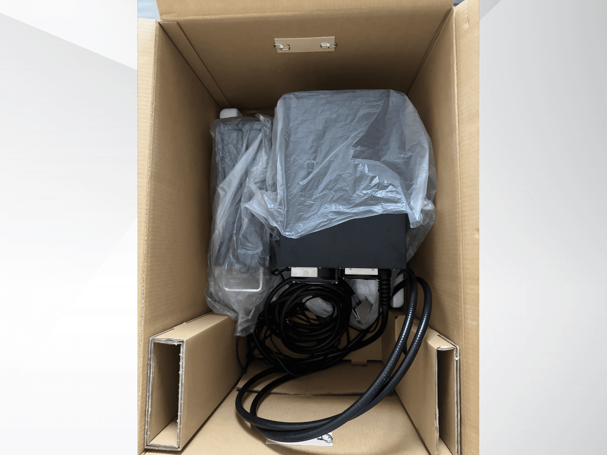Máquina de marcação a laser KEYENCE MD-X2500A numa caixa de cartão, parcialmente coberta com plástico, com os cabos e componentes visíveis.