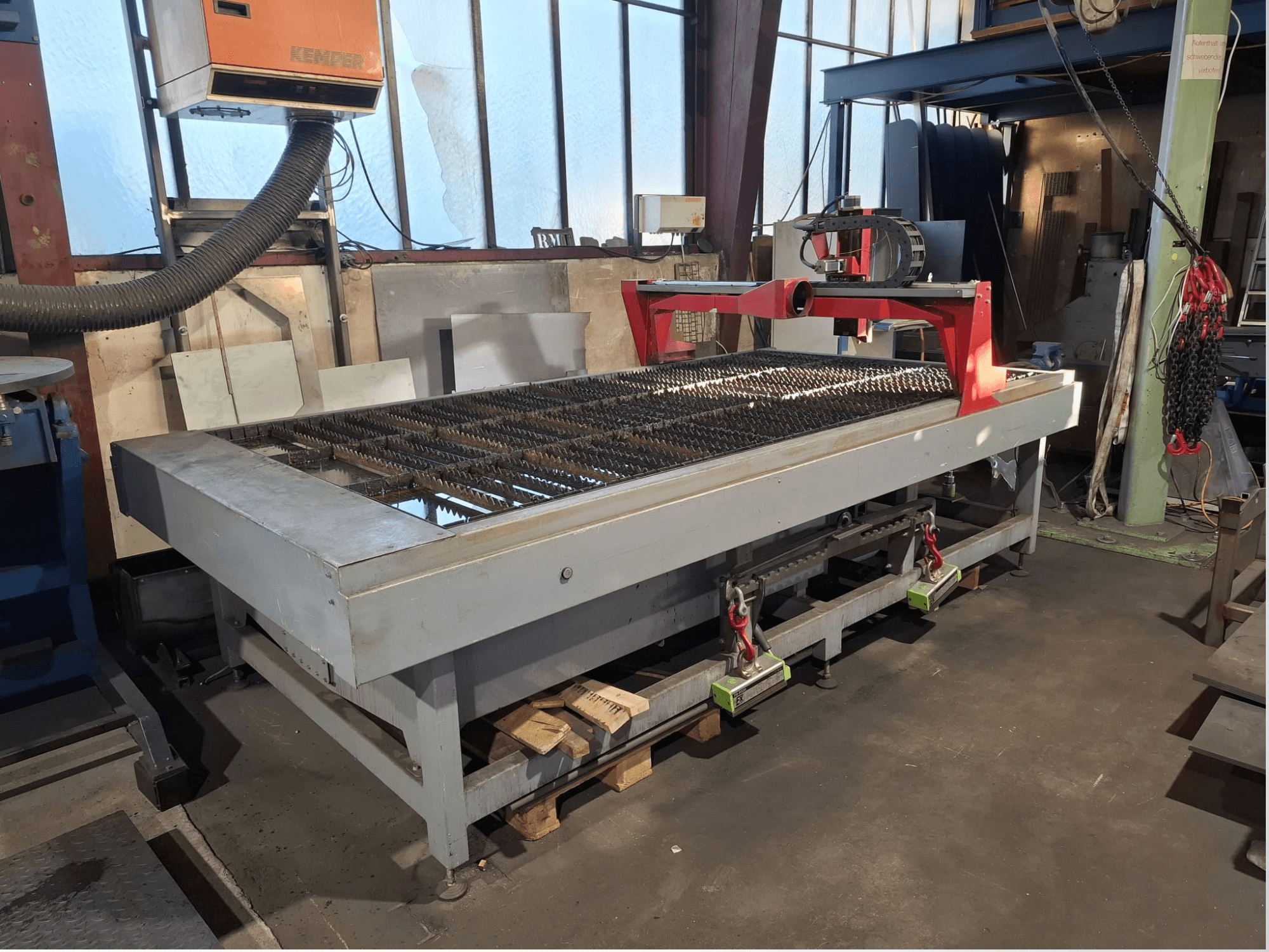Máquina de corte por plasma PLASMACUT 3015T, vista de perfil, com uma ampla mesa de corte com ripas metálicas e estrutura vermelha.