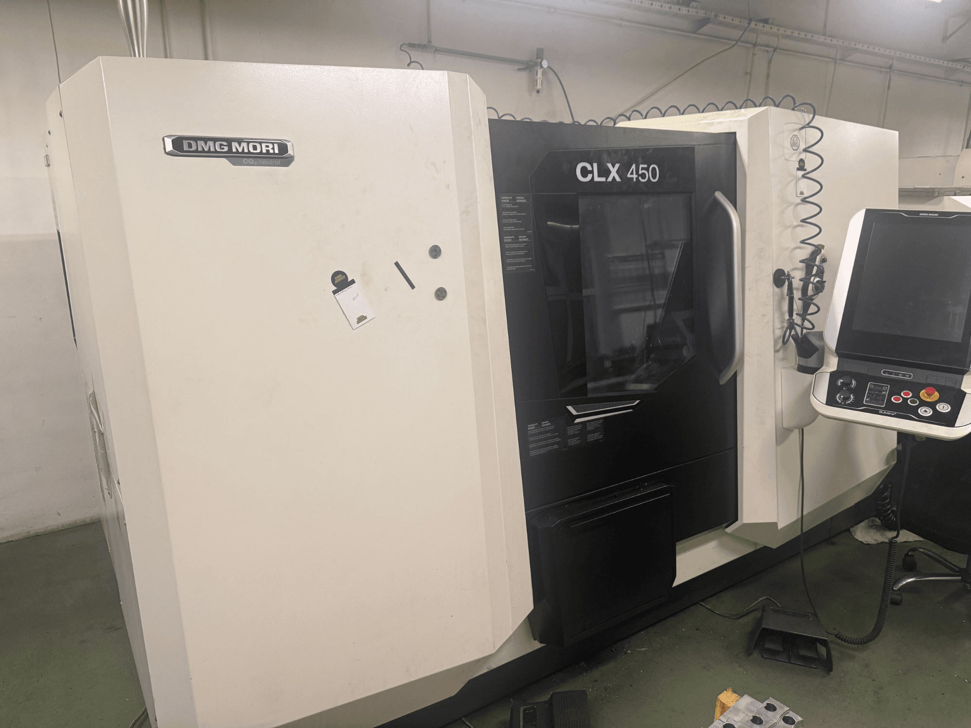Máquina CNC DMG MORI CLX 450, vista lateral com painel de controlo, botões operacionais visíveis e espaço de trabalho limpo.