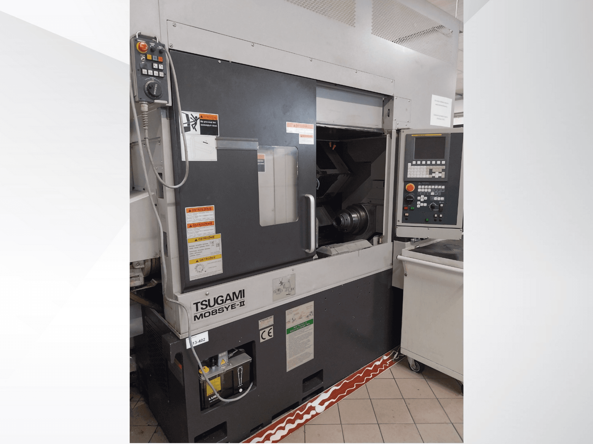 Torno CNC Tsugami M08SY-II, vista frontal, mostrando o painel de controlo, o fuso e a área de carga. Inclui avisos de segurança e etiqueta da marca.
