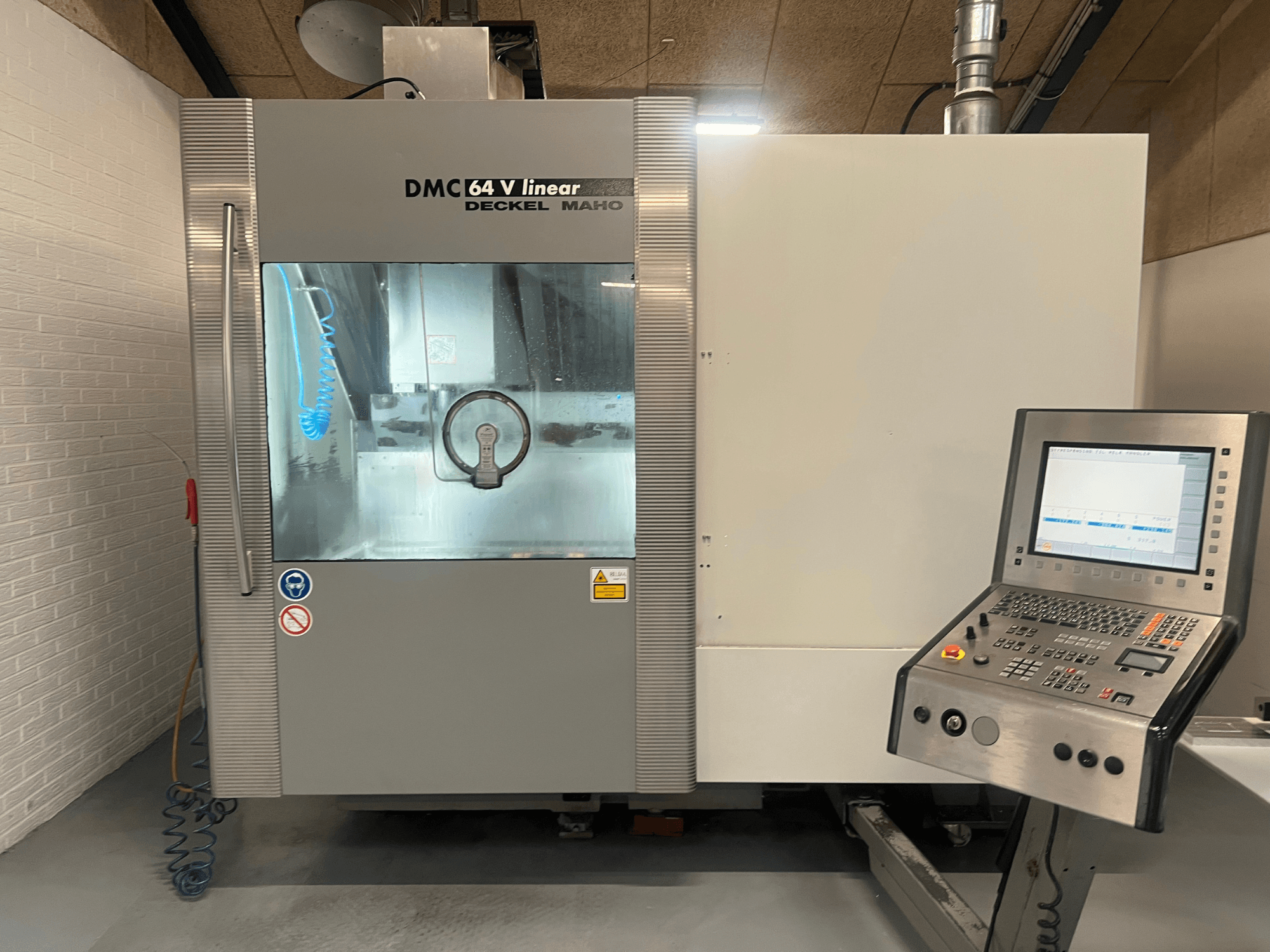 Máquina CNC linear DECKEL MAHO DMC 64 V, vista frontal com painel de controlo e mangueira de refrigeração visíveis.
