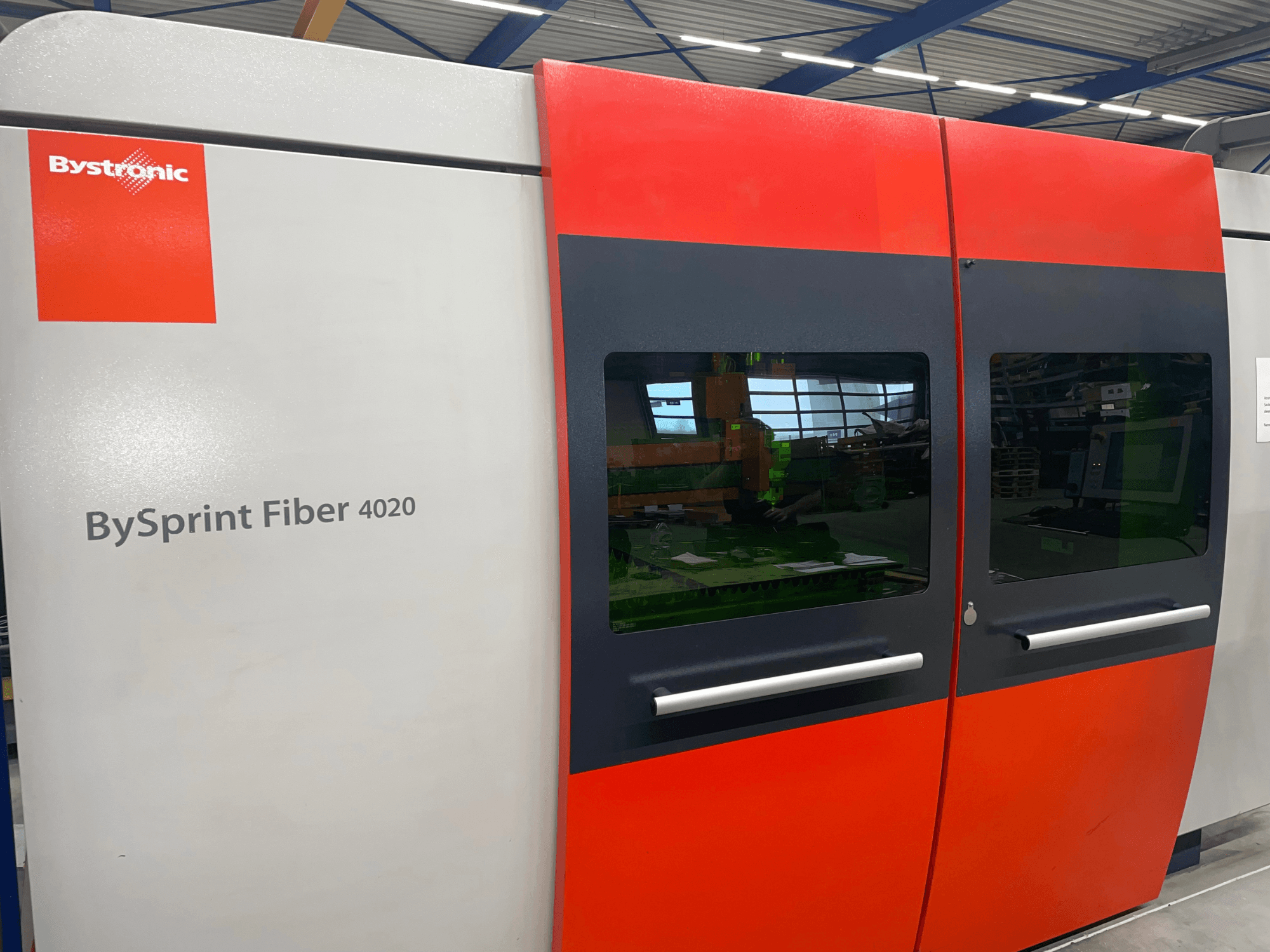 Bystronic BySprint Fiber 4020 em vista frontal, com um design de painel cinzento e vermelho com grandes janelas e interface de controlo visível no interior.