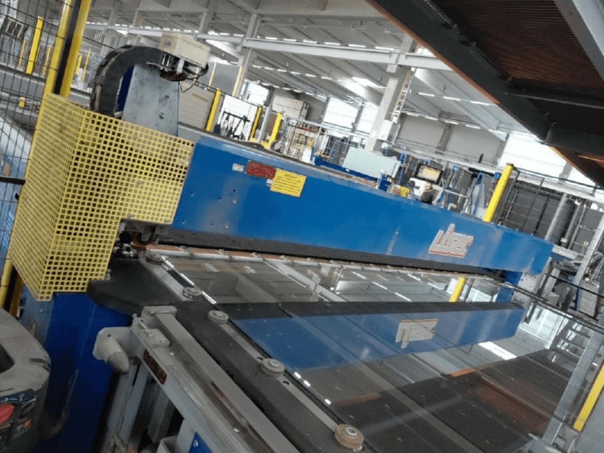 Vista frontal da linha de corte combinada de vidro VSG e vidro float da LISEC, com uma ferramenta de corte azul e uma rede de proteção.