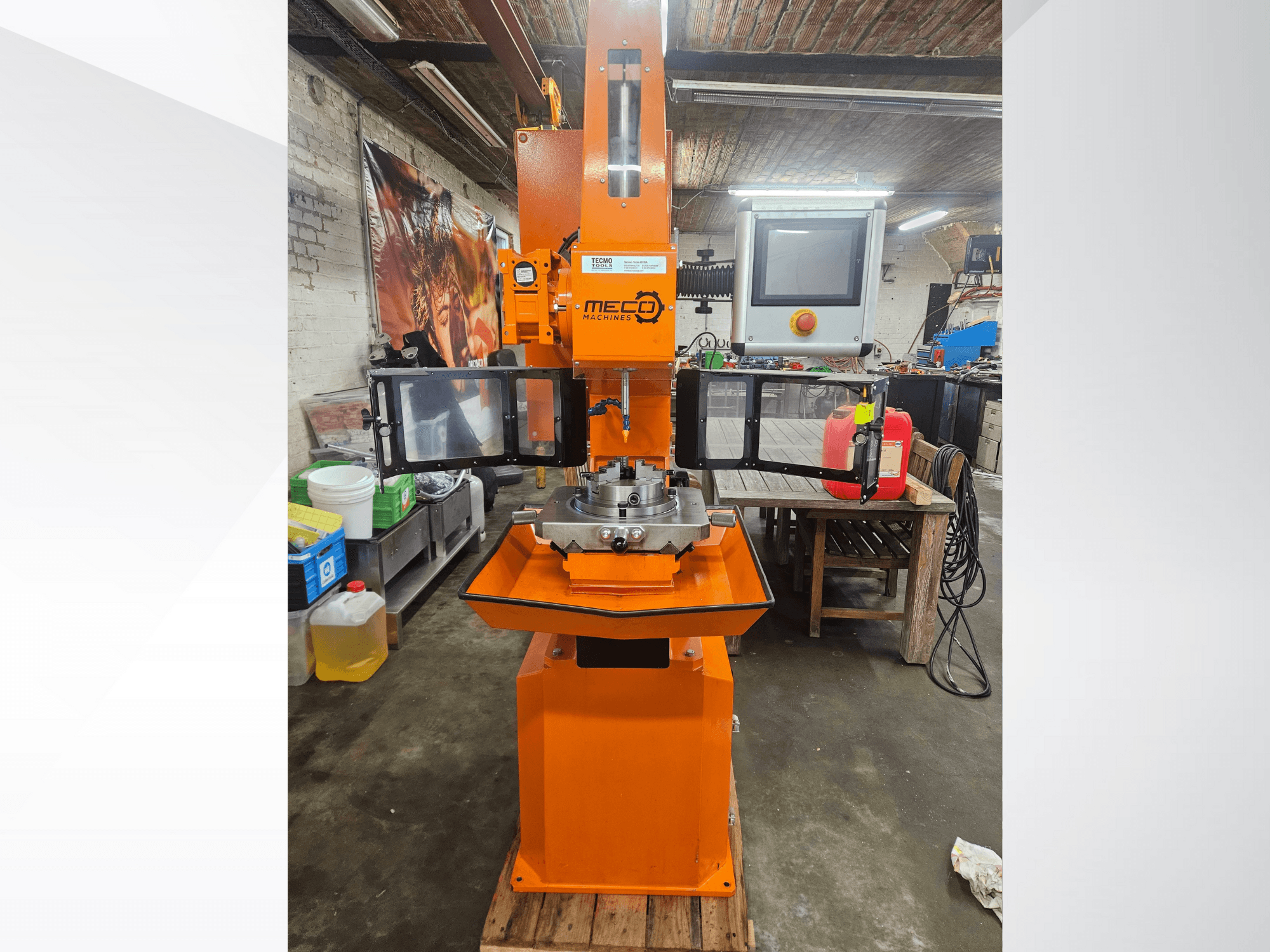 Fresadora MEC laranja, vista frontal, com painel de controlo e mesa de trabalho, situada numa oficina com ferramentas e materiais.
