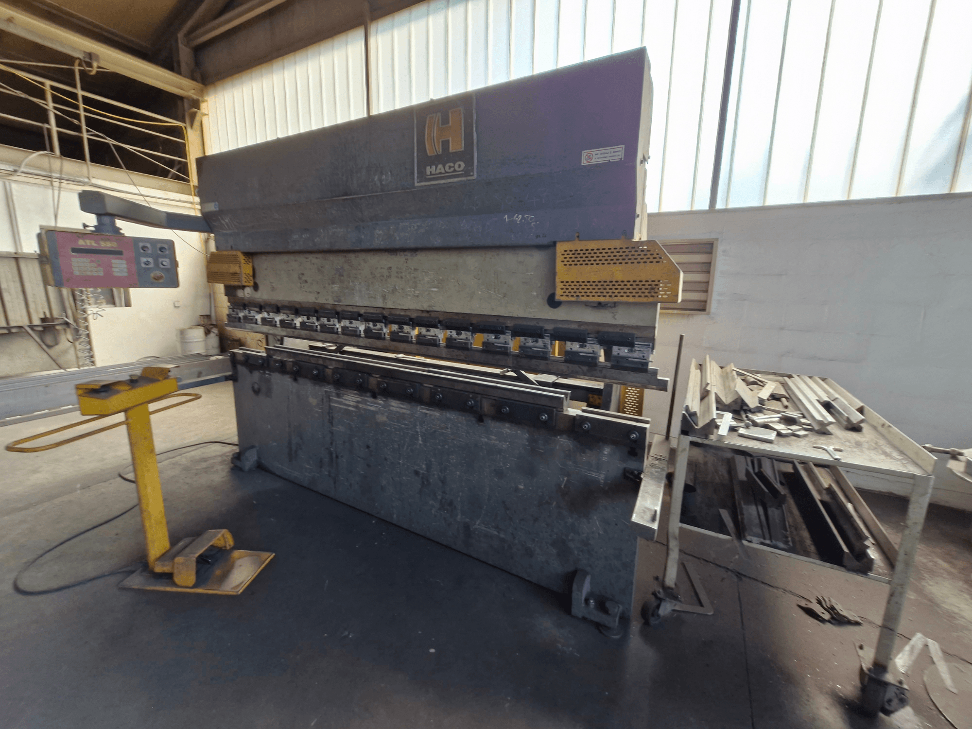 Prensa dobradeira HACO PPM 30135 b numa oficina, vista frontal mostrando o painel de controlo e sucata de metal numa mesa ao lado.