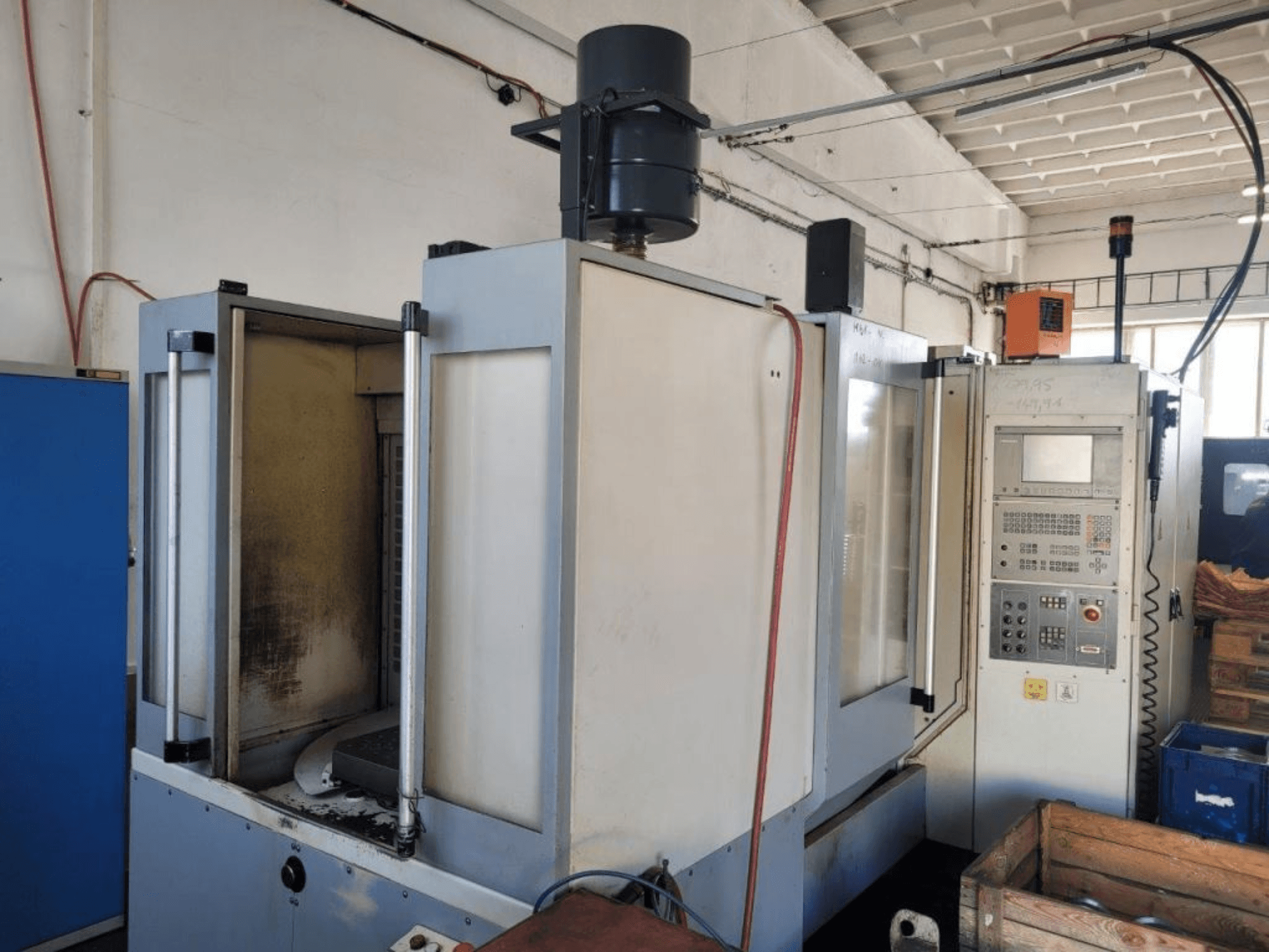 Fresadora industrial CNC com painel de controlo, vista lateral, mostrando a caixa e a sujidade visível nas superfícies.