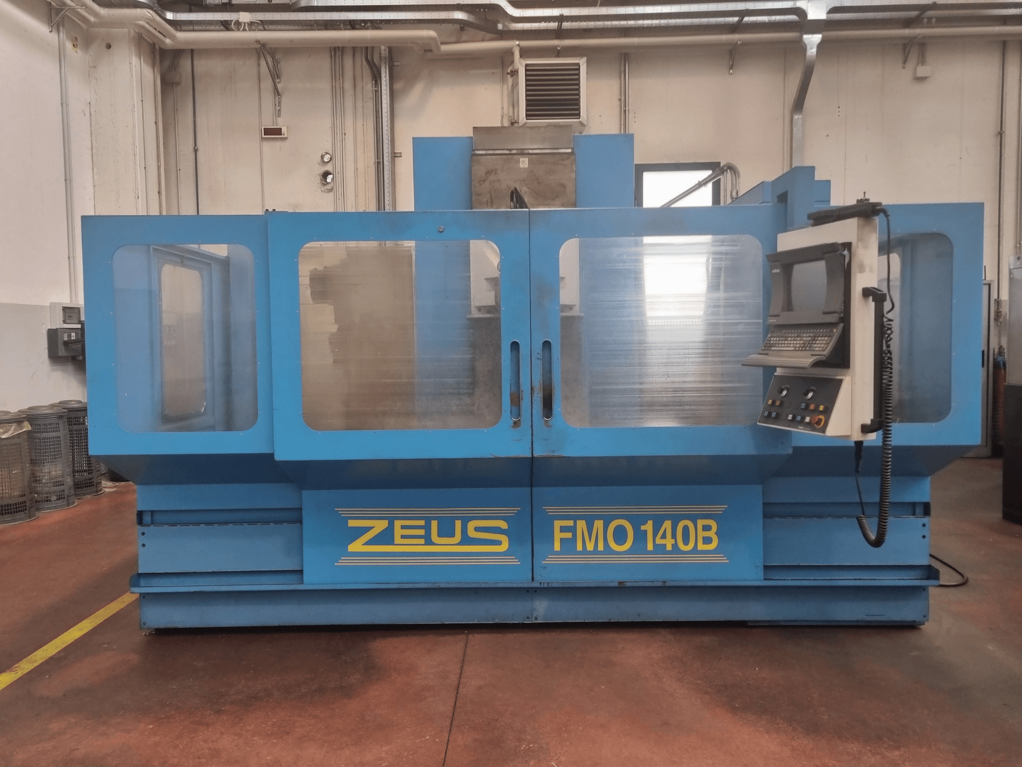 Máquina Zeus FMO 140B em azul, vista frontal; possui painel de controlo e grandes painéis transparentes para maior visibilidade.