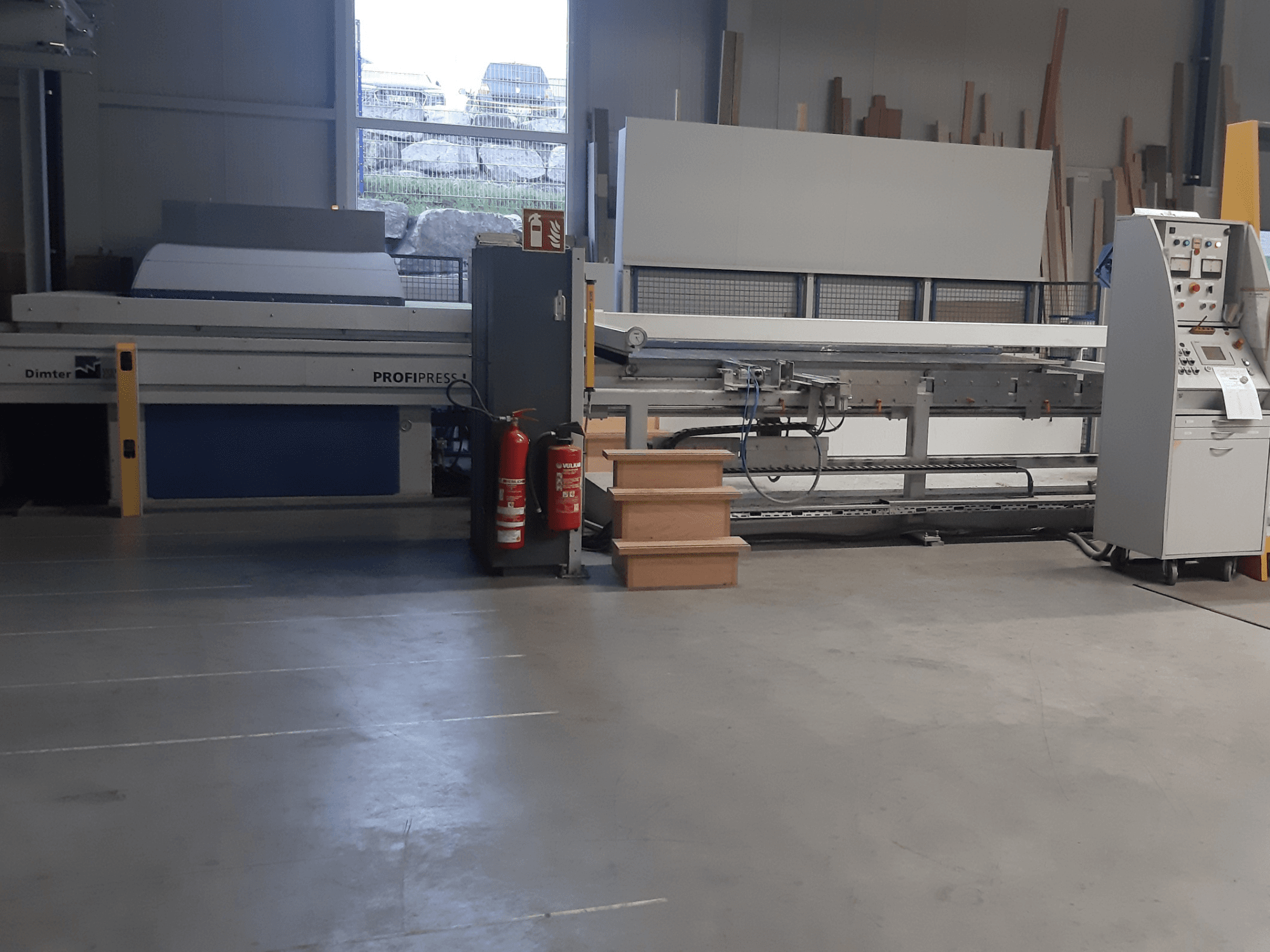 Máquina Dimter ProfiPress numa oficina, vista de frente, com painel de controlo e extintores de incêndio nas proximidades.