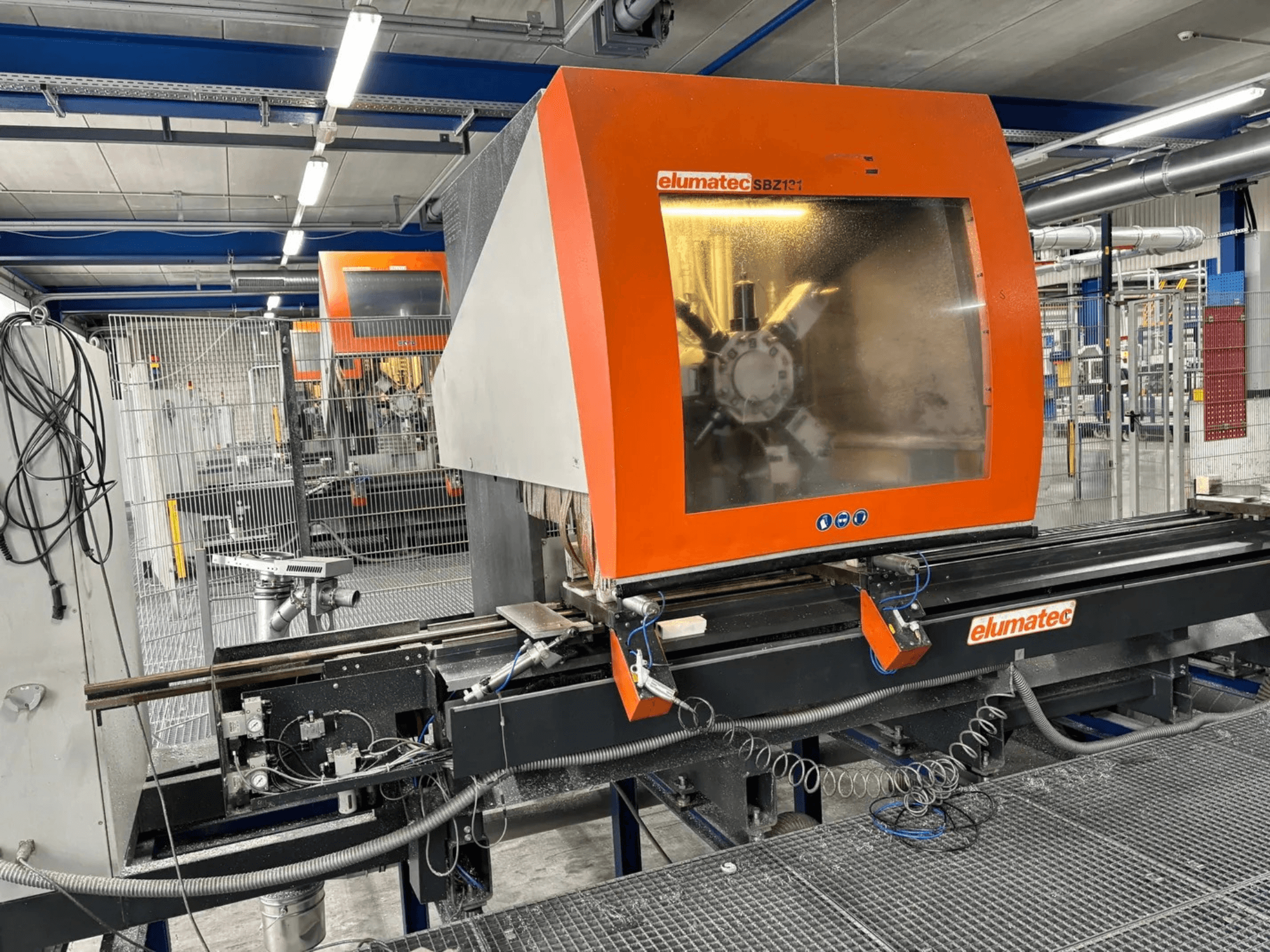 Centro de maquinação vertical Elumatec SBZ 131, vista frontal, mostrando o painel de controlo, detalhes da máquina e ambiente de trabalho circundante.