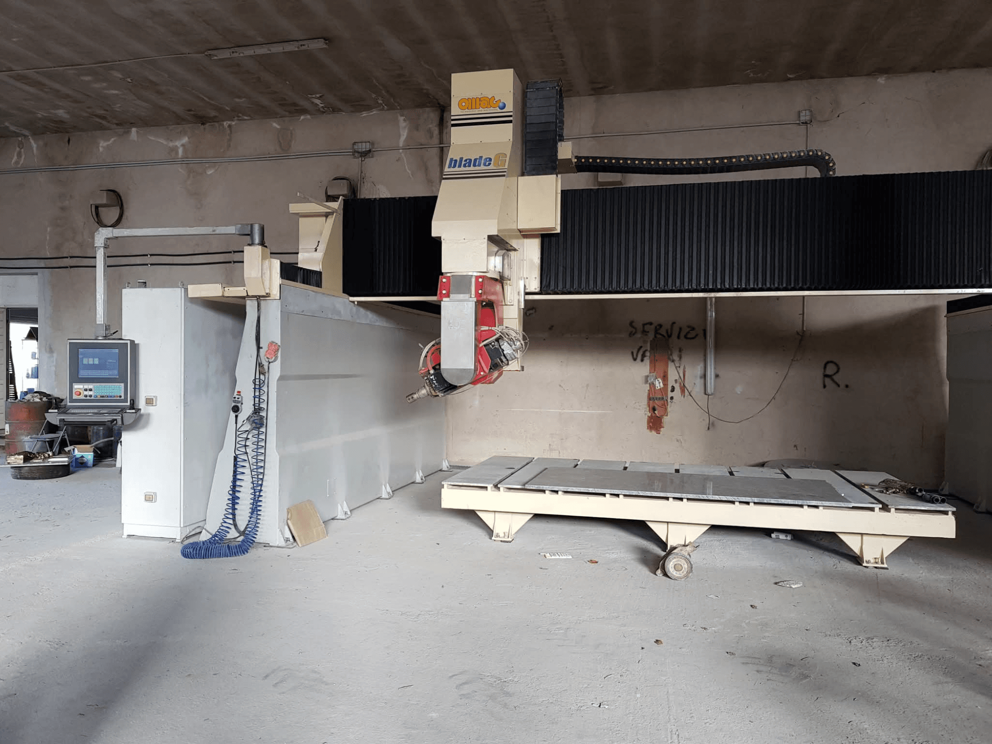 Fresadora de pórtico OMAG Blade G numa oficina, vista frontal com painel de controlo e grande mesa de fresagem visível.