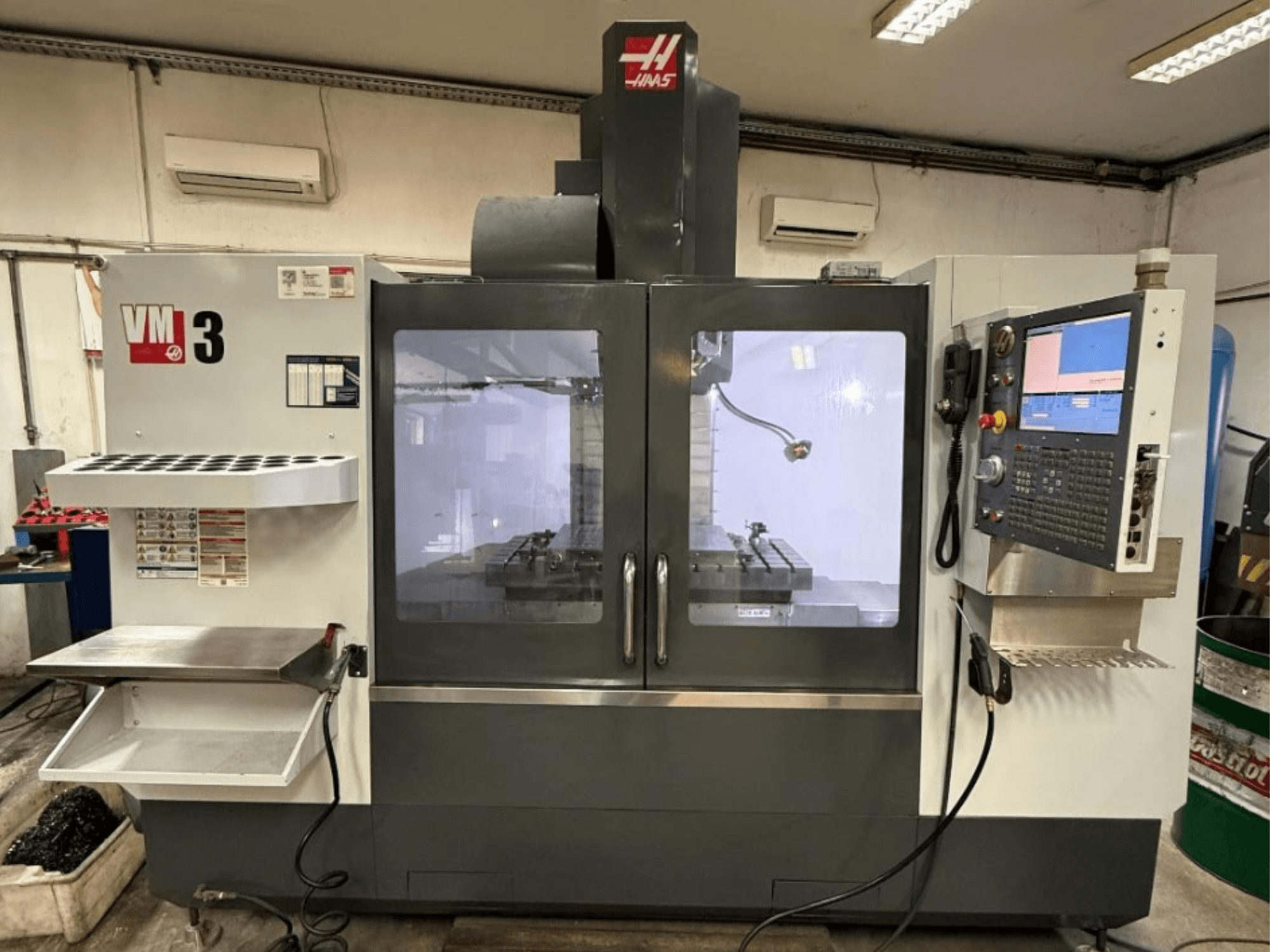 Centro de maquinagem vertical Haas VM-3, visto de frente, com um painel de controlo de grandes dimensões e uma área de trabalho visível com as ferramentas.