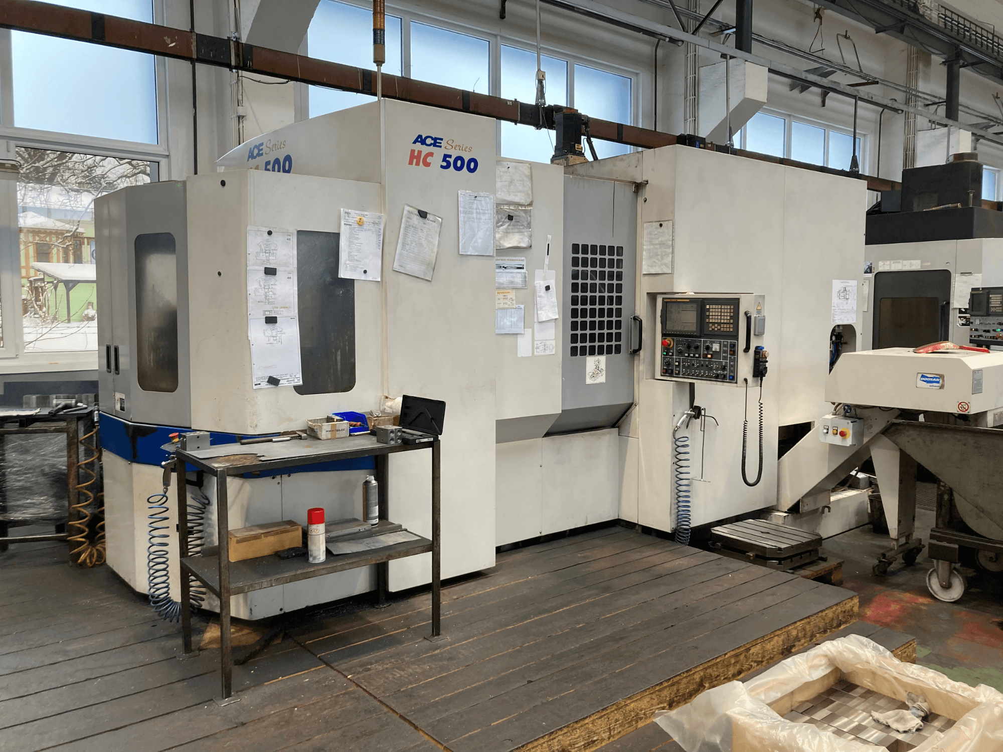 Centro de maquinação horizontal DOOSAN ACE HC-500, vista frontal; possui painel de controlo, armazenamento múltiplo de ferramentas e ambiente industrial.