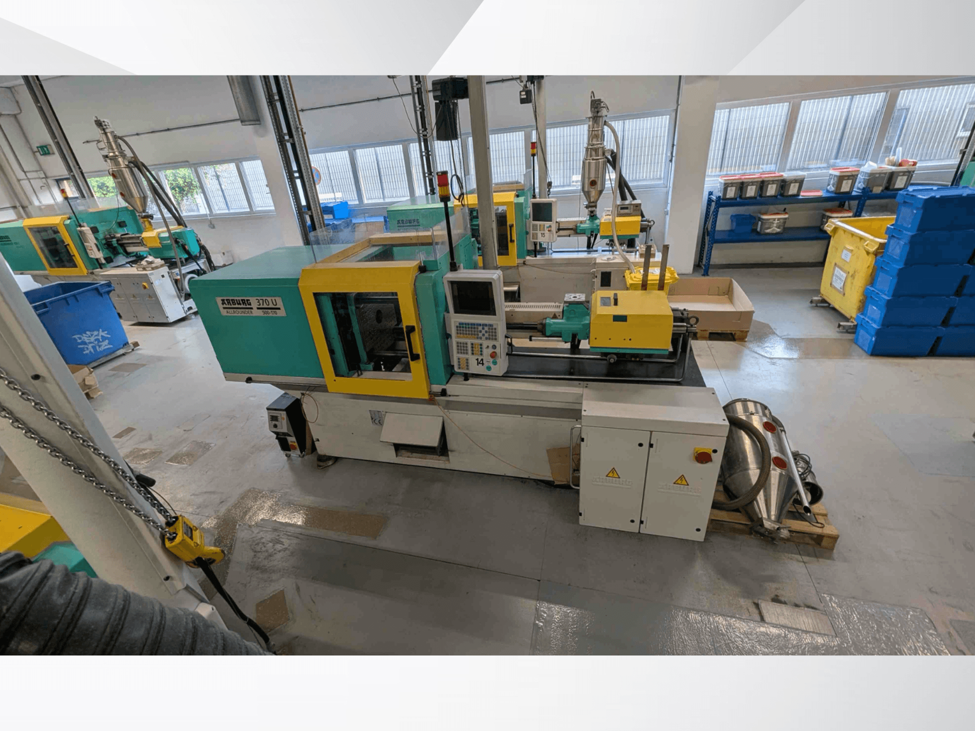 Vista frontal da máquina de moldagem por injeção vertical Arburg 370 U 500-170, com o painel de controlo e os componentes da máquina, numa oficina.