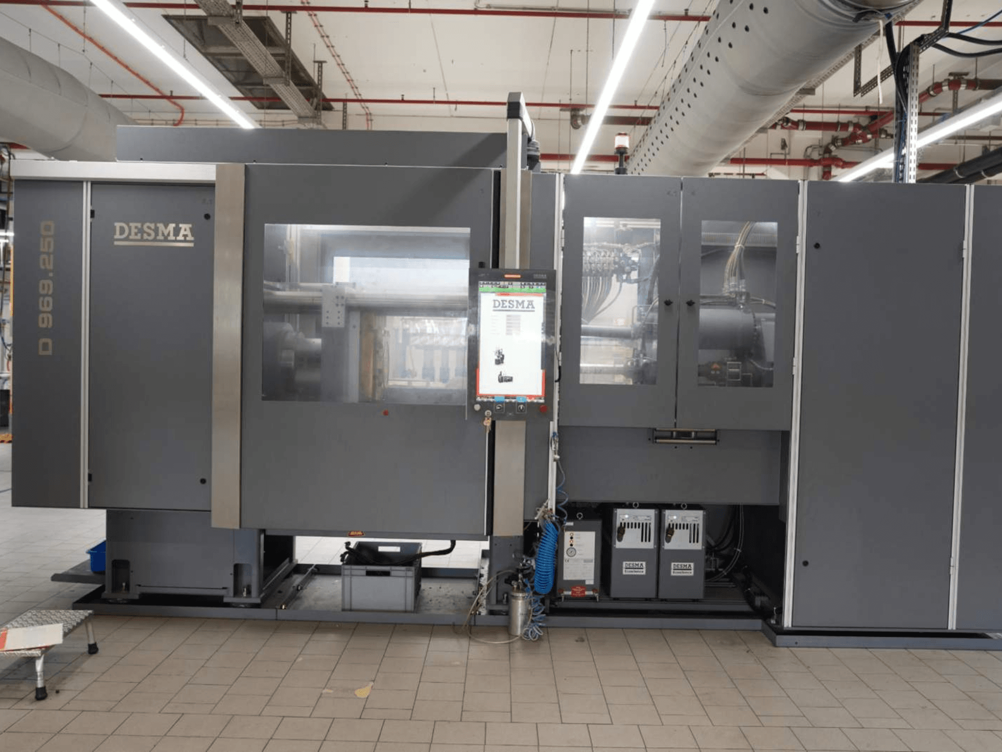 Máquina de moldagem por injeção vertical Kloeckner Desma D 969.250 Z (S3) numa fábrica, vista frontal com painel de controlo.