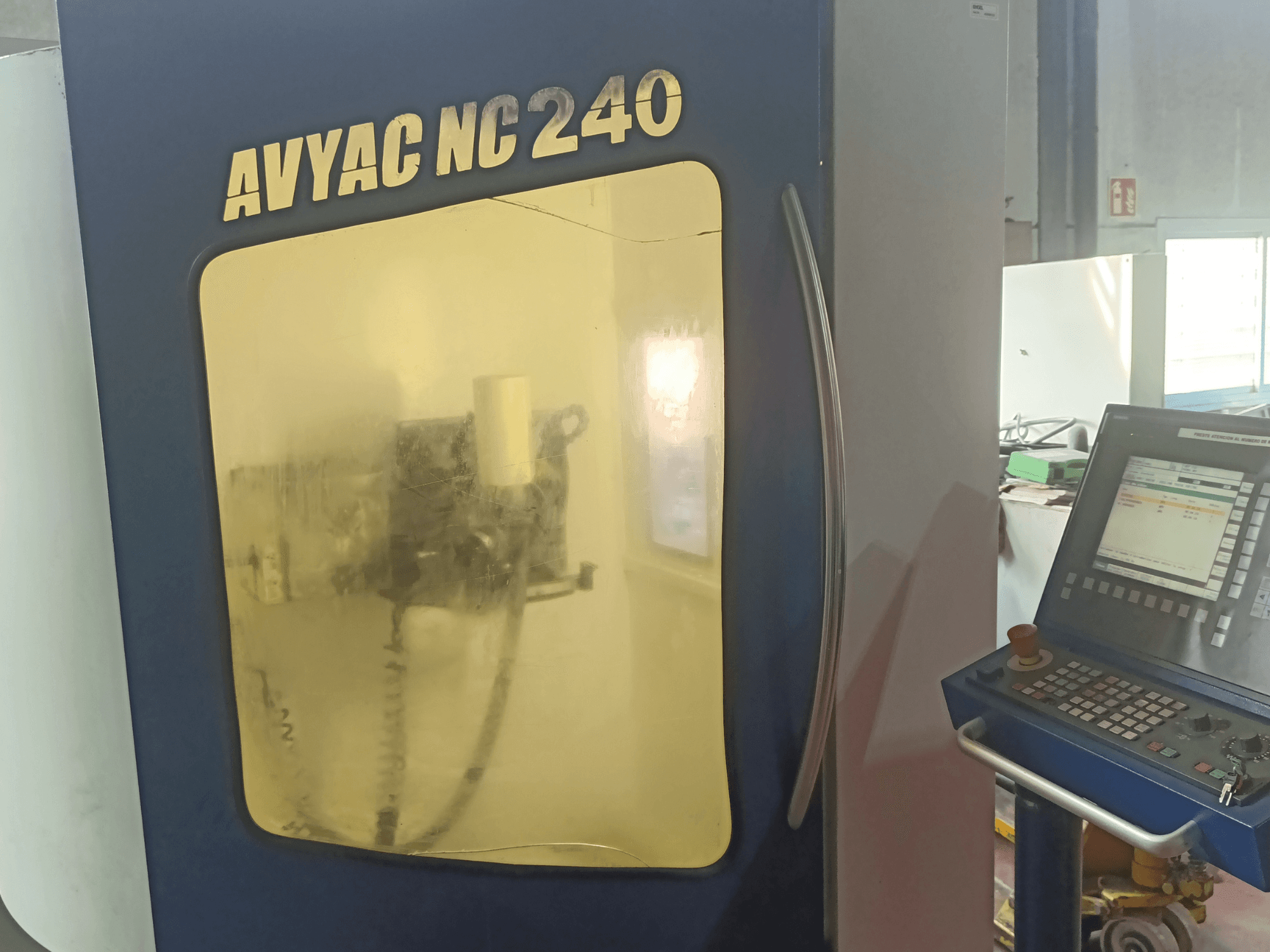 Máquina de retificação cilíndrica AVYAC NC240, vista lateral mostrando o painel de controlo e a área de retificação parcialmente visível através da janela.