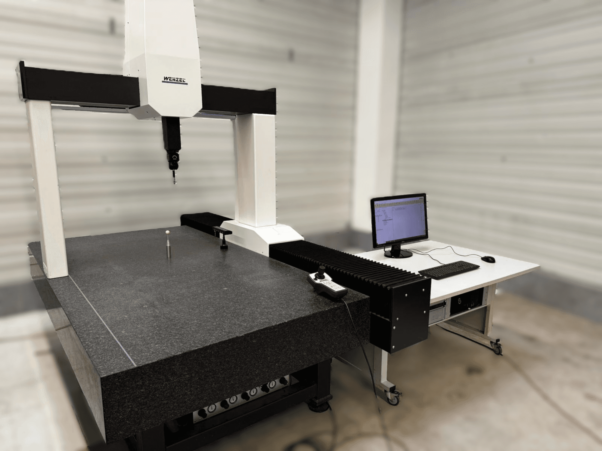 CMM XO 87 da Wenzel em vista frontal, com uma sonda de medição e uma mesa de granito com um computador instalado ao lado.