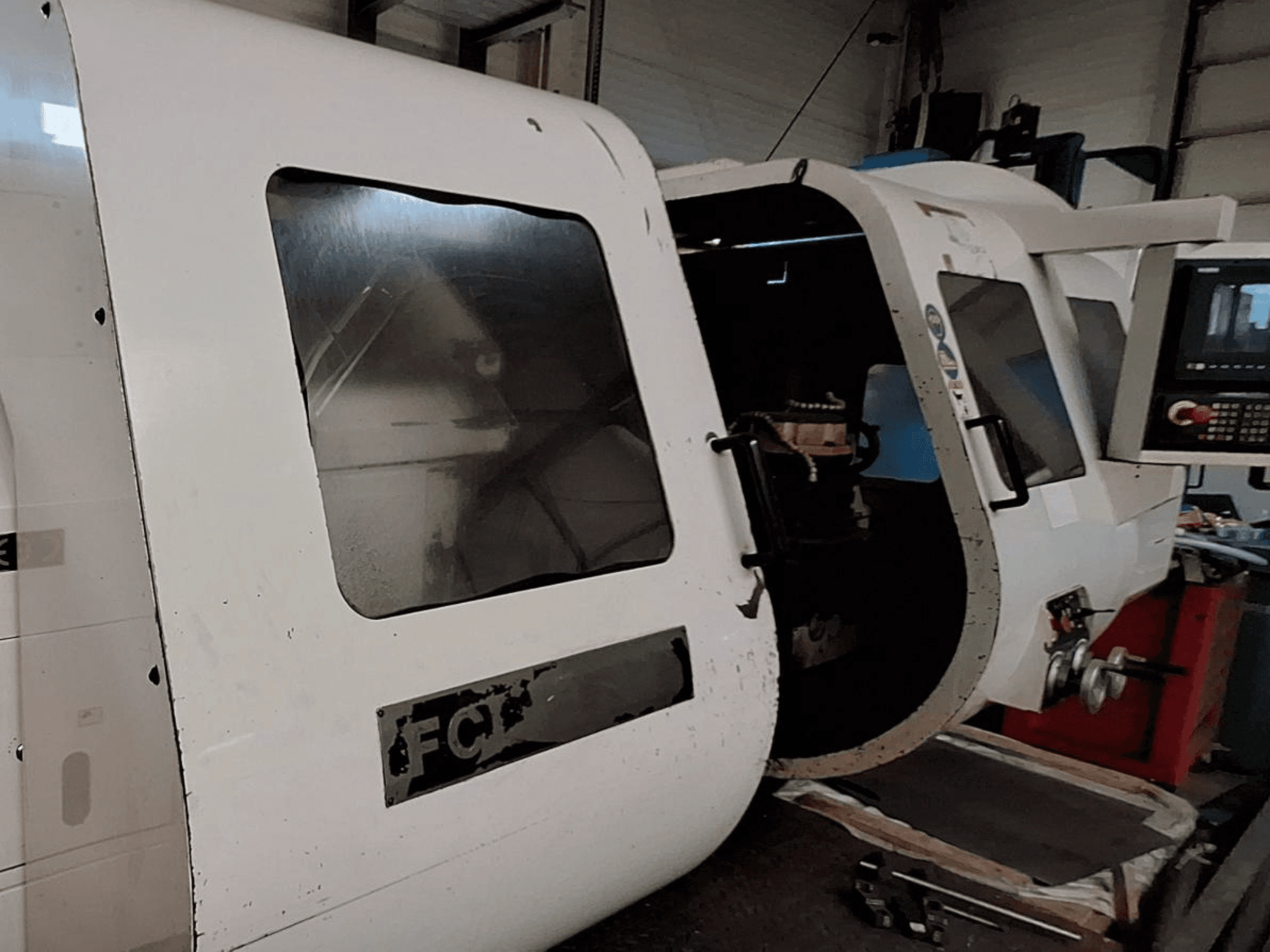 Máquina CNC branca com painel de controlo visível e porta aberta, mostrando componentes interiores; vista frontal. Marca: FCT.