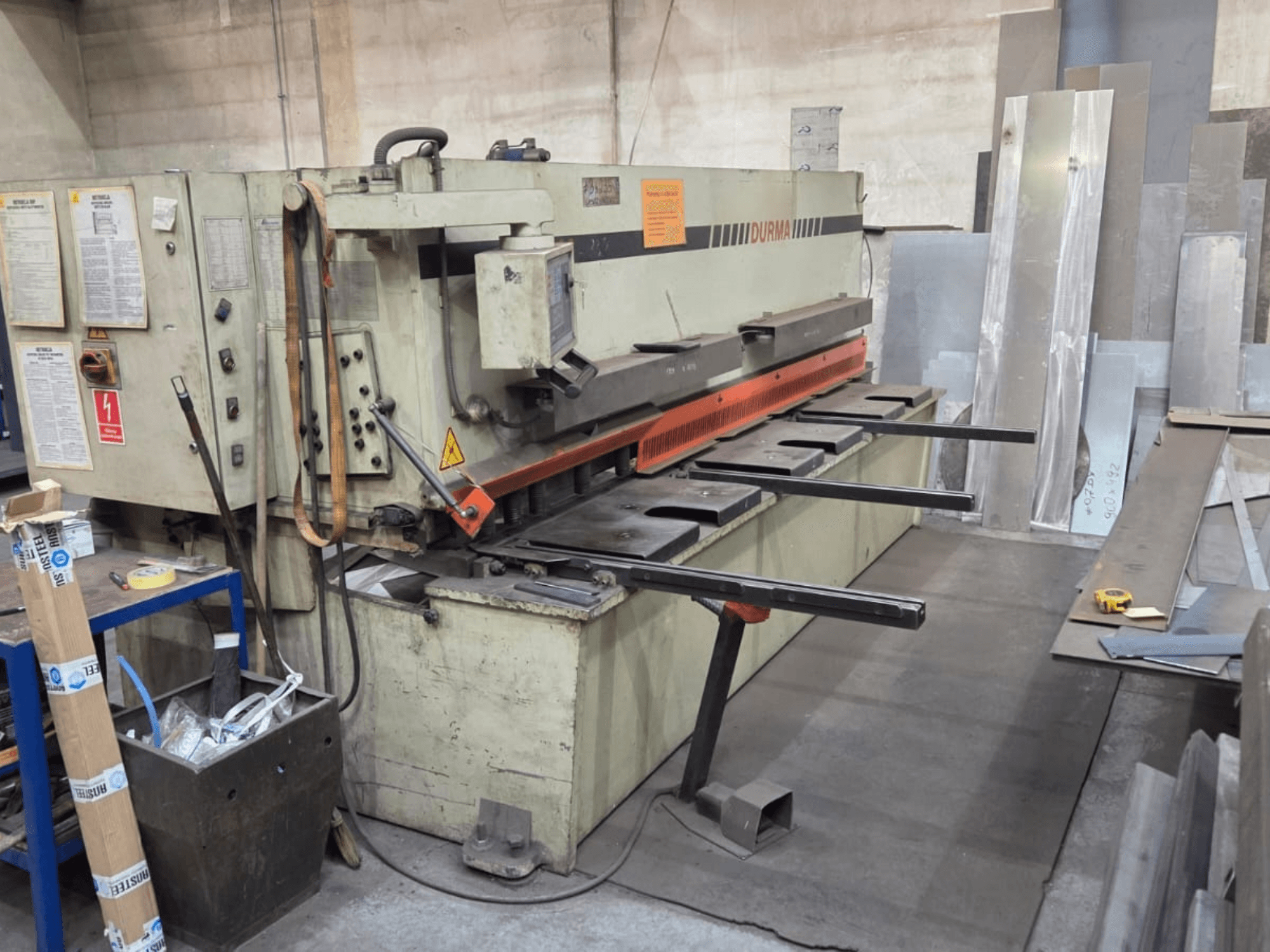 Máquina de corte hidráulica Durma SB 3060, vista frontal, mostrando os controlos, o disco de corte e as chapas metálicas na área de trabalho.