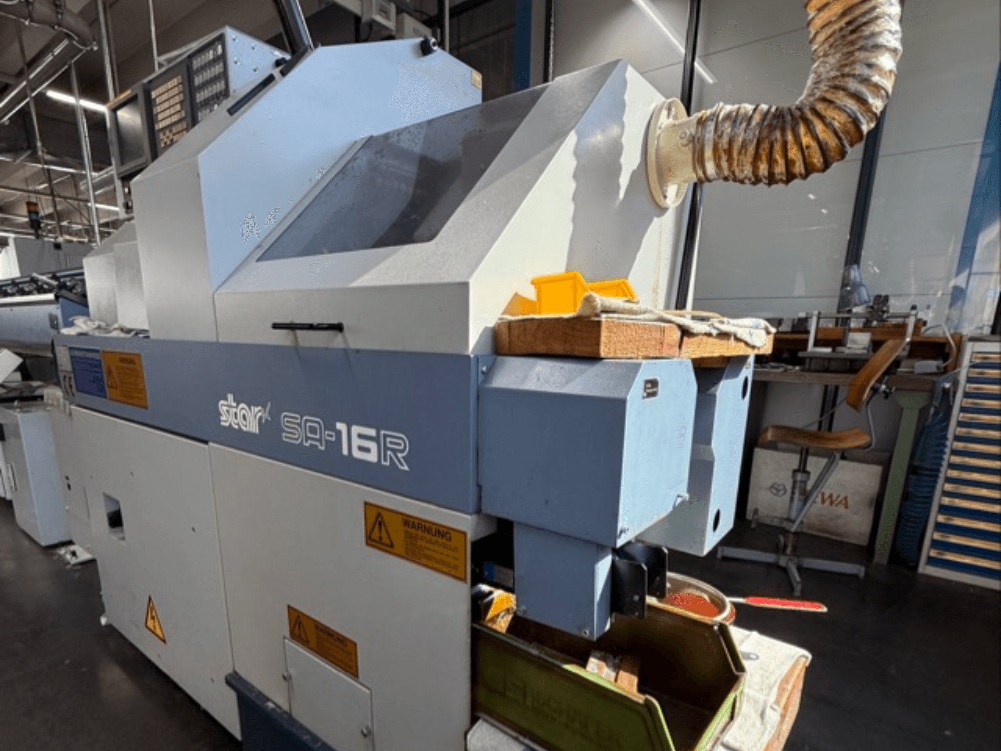 Máquina Stark SA-16R vista de frente, com um escape cónico e um espaço de trabalho com ferramentas amarelas e etiquetas de aviso.