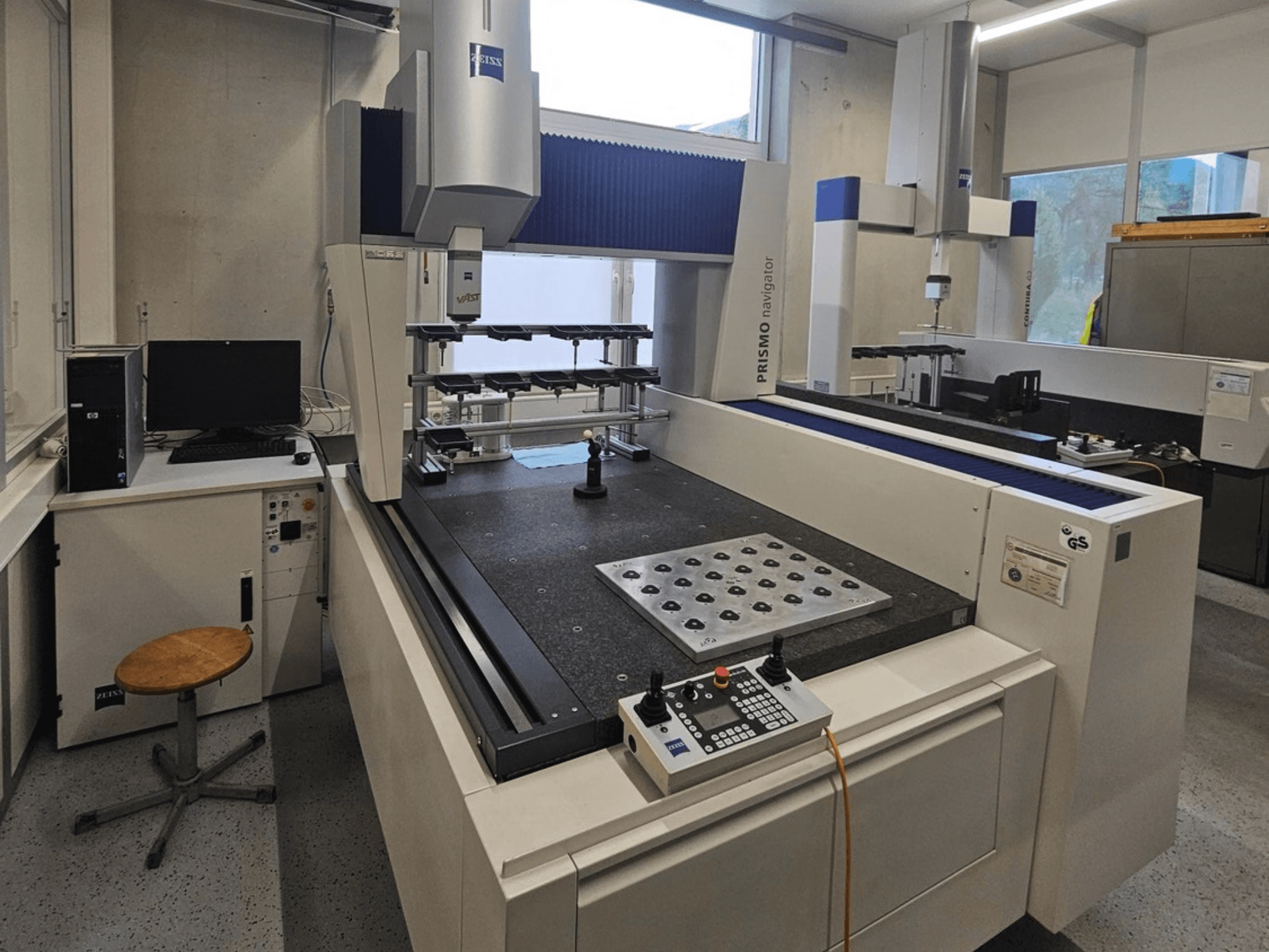 MMC ZEISS Prismo Navigator 7 num laboratório, vista frontal que mostra o painel de controlo, a mesa de trabalho e o monitor.