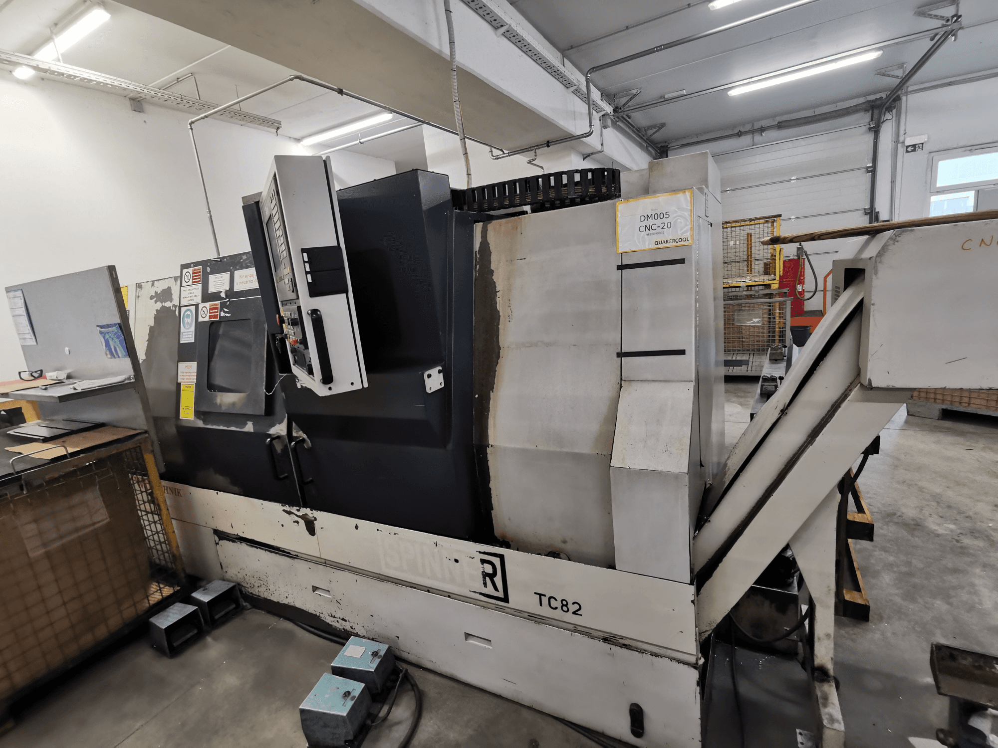 Máquina CNC, marca Spinner, modelo TC82, vista lateral mostrando o painel de controlo e a calha de remoção de sucata numa oficina.