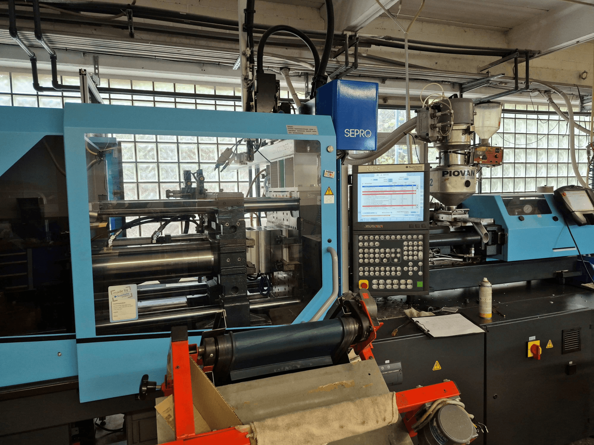 Máquina de moldagem por injeção hidráulica SUMITOMO SHI DEMAG Systec 120/470-430, vista frontal com o painel de controlo e o sistema de alimentação visíveis.