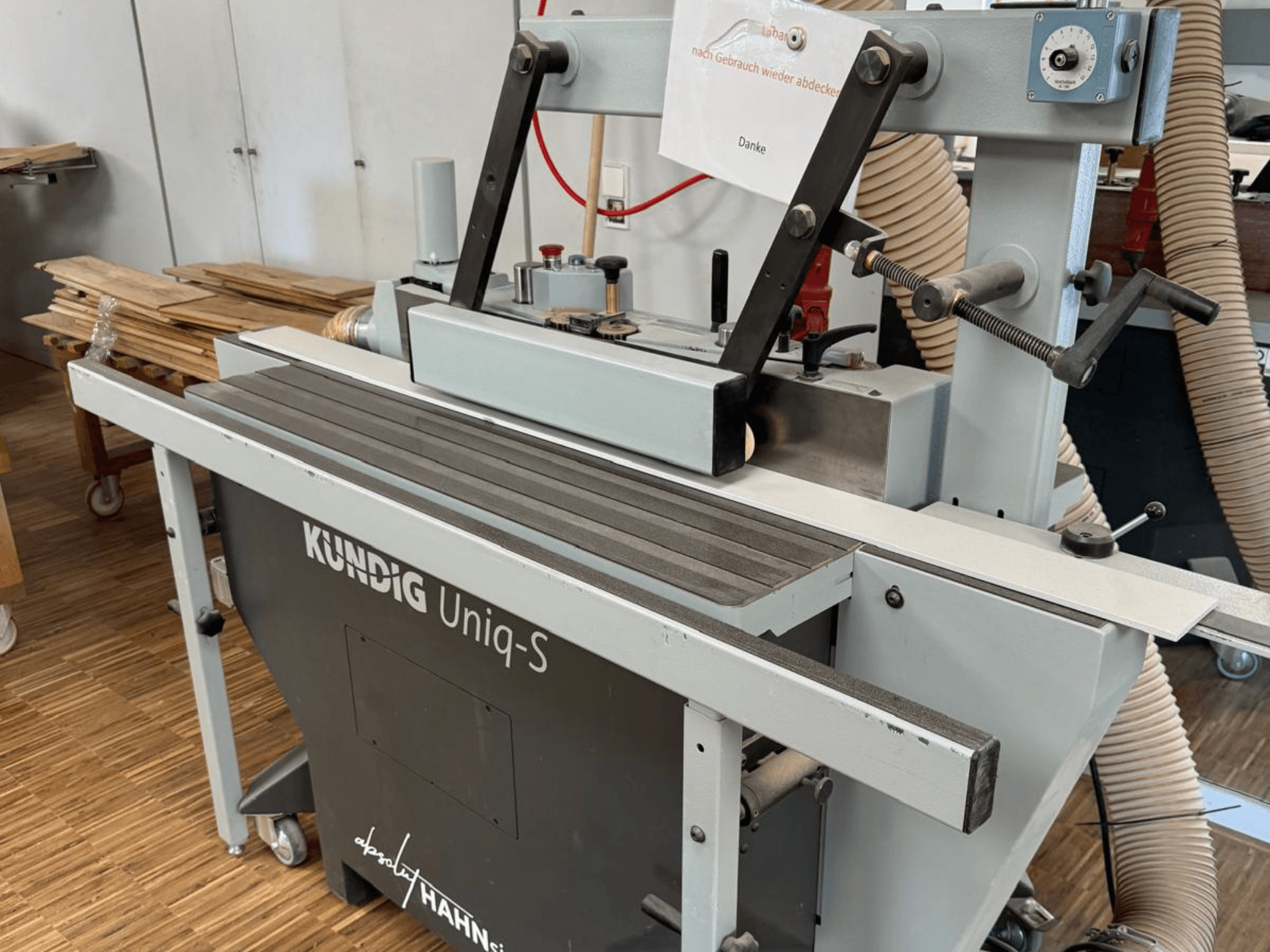 Lixadeira de cinta Kundig UNIQ-S numa oficina, vista lateral mostrando a cinta de lixa e os braços de suporte ajustáveis.