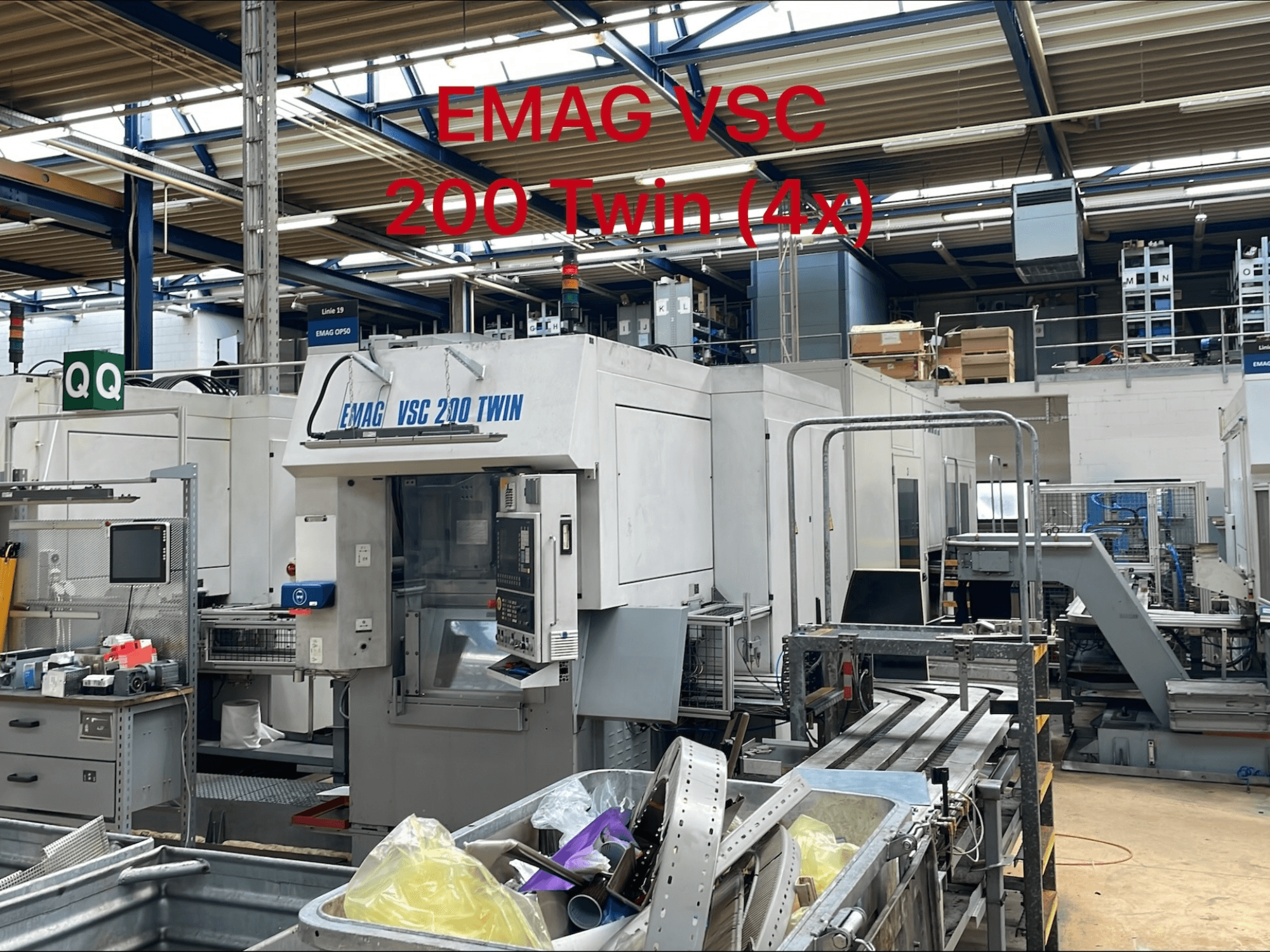 Máquina de torneamento vertical EMAG VSC 200 TWIN numa fábrica, vista frontal mostrando os controlos e a área de armazenamento de ferramentas.