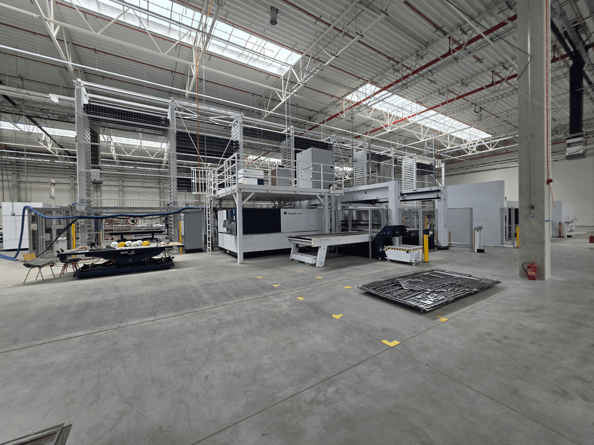 Sistema automatizado de produção de chapa metálica da TRUMPF, vista lateral que mostra as máquinas, o espaço de trabalho e as ferramentas num grande ambiente industrial.