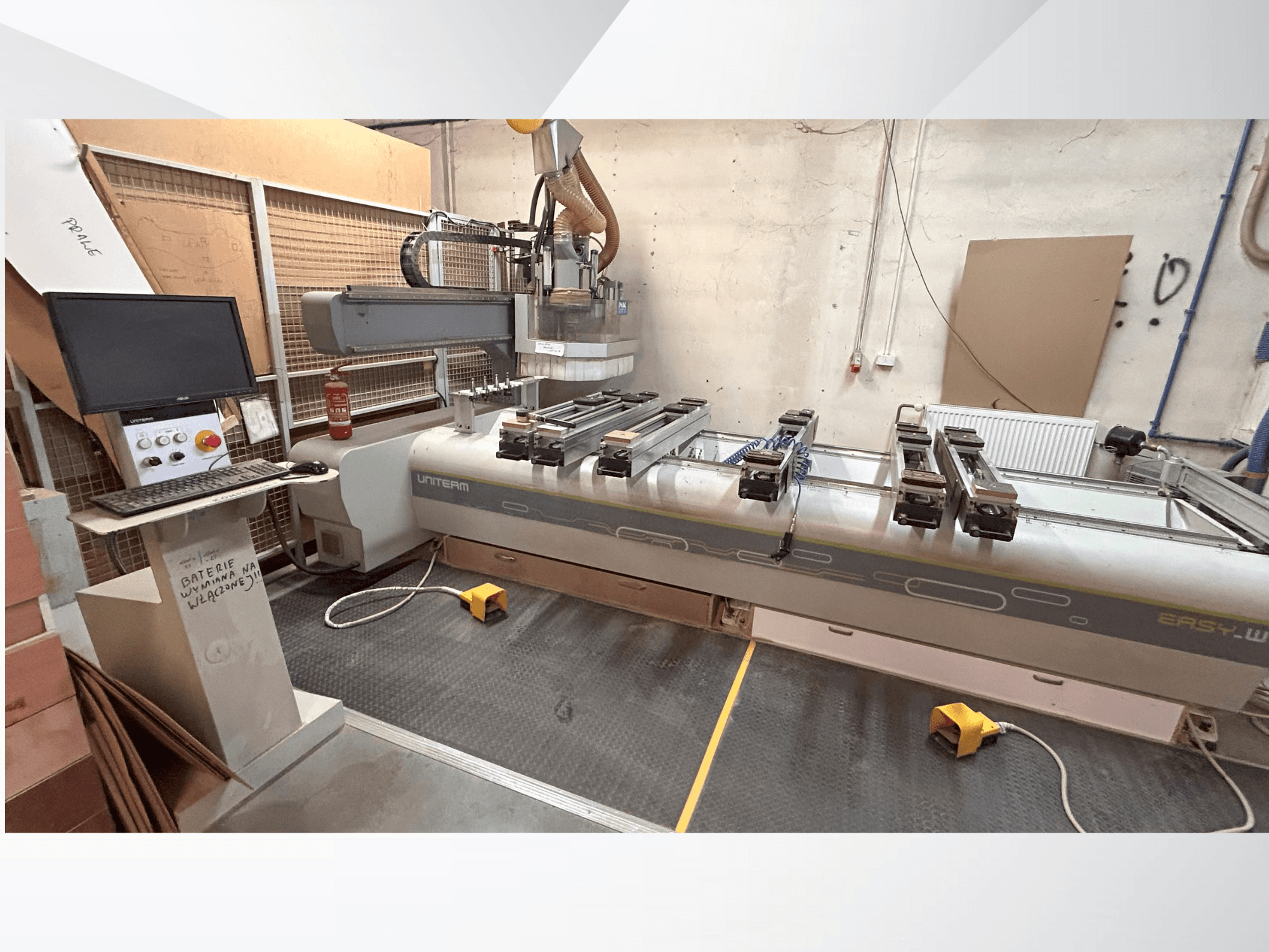 Vista frontal de uma máquina CNC UNITEM EASY-W, com um painel de controlo, um monitor e peças fixas na mesa de trabalho.