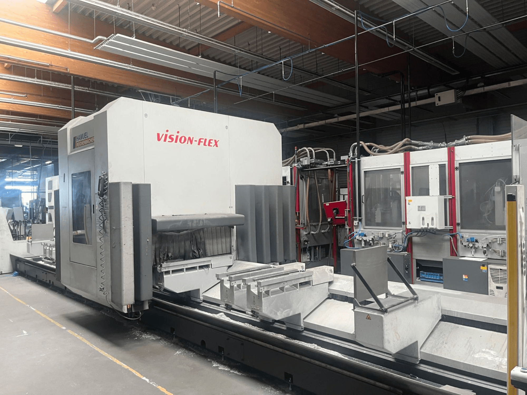 Centro de maquinagem vertical Hamuel Reichenbacher Vision Flex, vista lateral que mostra a área de trabalho e os comandos num ambiente industrial.