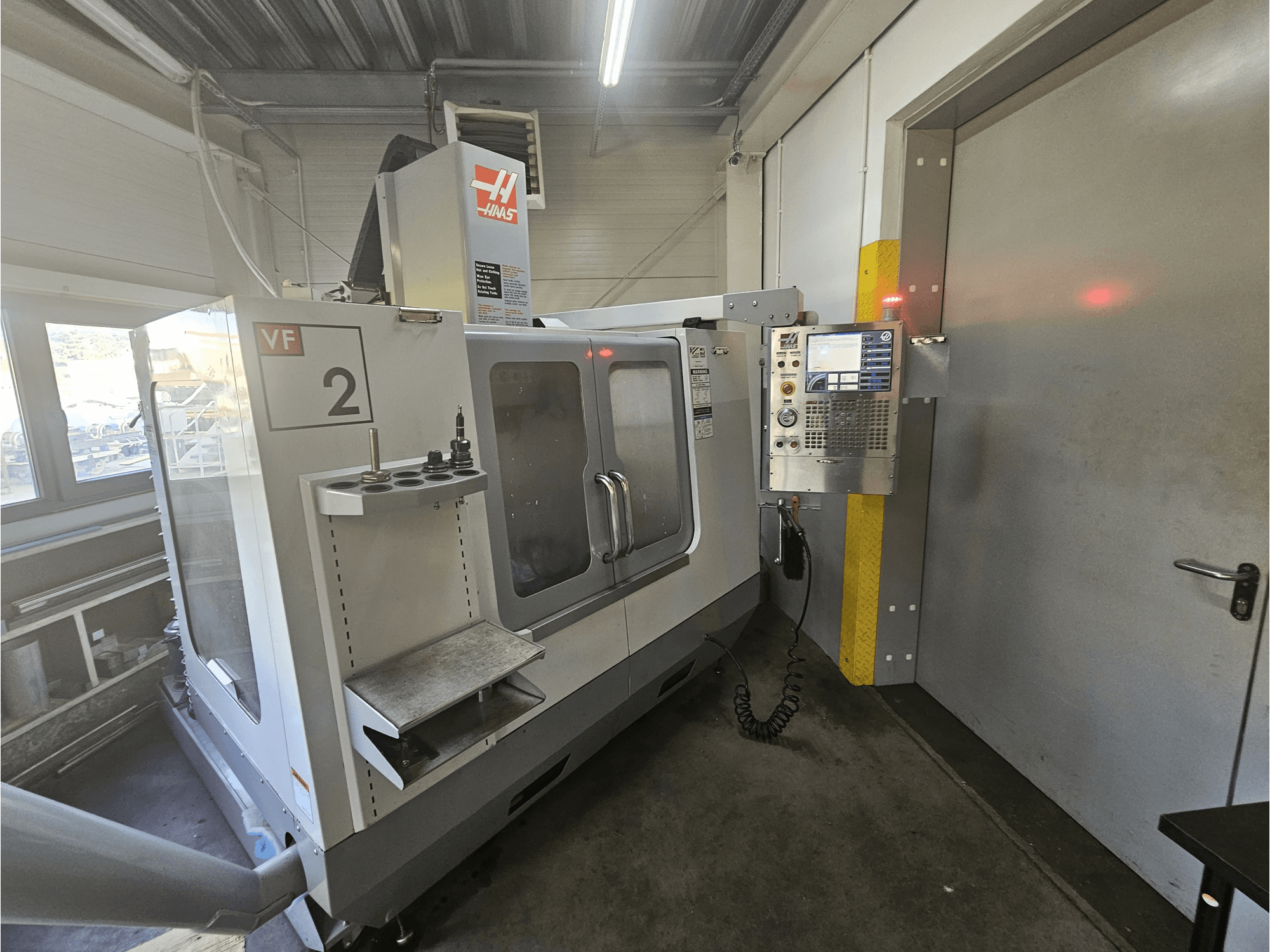 Fresadora CNC Haas VF-2, vista frontal, mostrando o painel de controlo, suportes de ferramentas e uma janela transparente na área de trabalho.