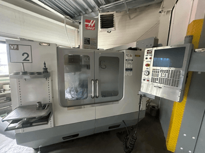 Máquina CNC Haas VF-2, vista frontal, com controlos, suporte de ferramentas e portas transparentes com ferramentas visíveis no interior do armário.