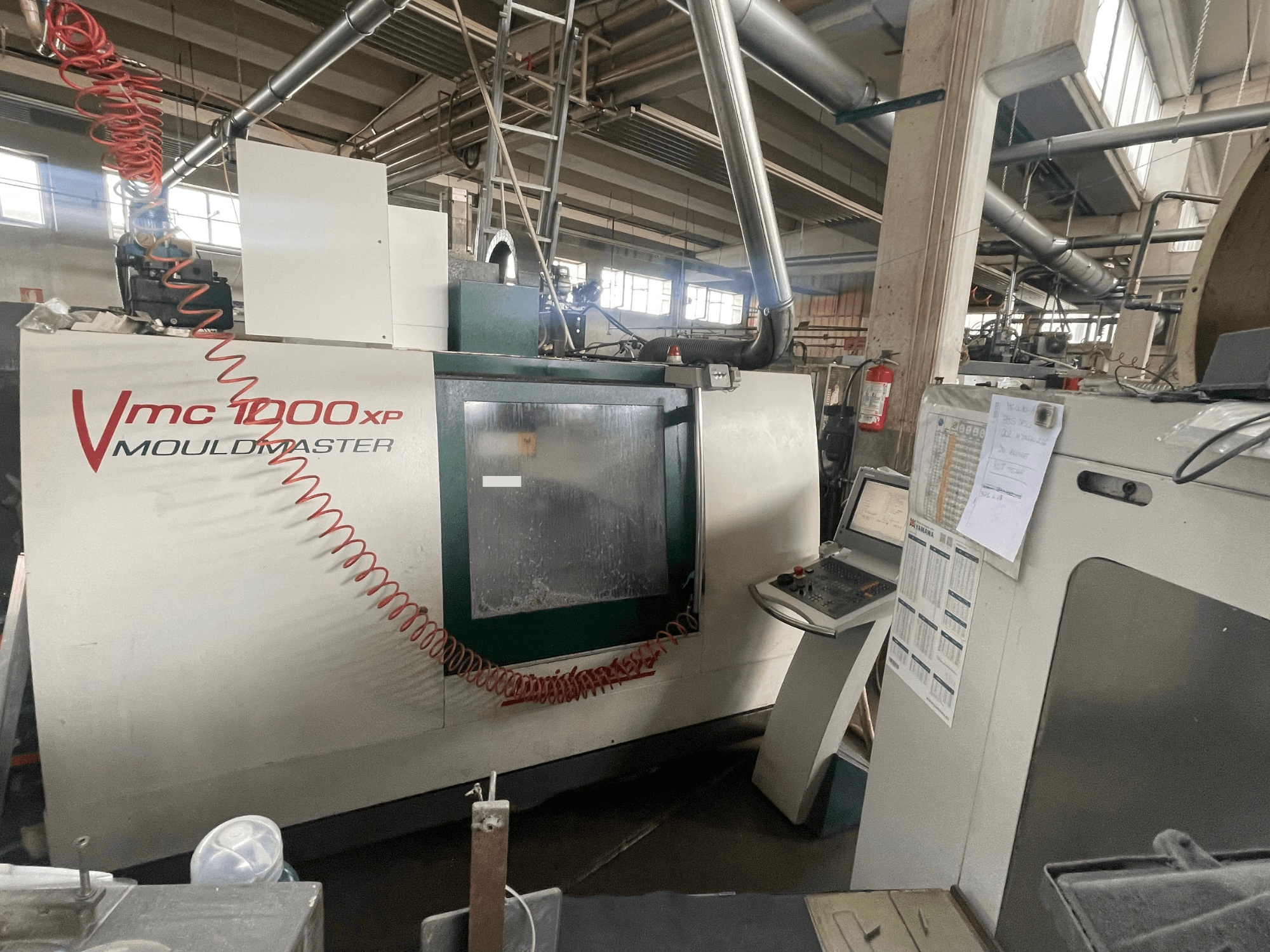 Centro de maquinagem vertical Bridgeport VMC 1000, vista frontal, mostrando o painel de controlo e os detalhes da máquina num ambiente industrial.