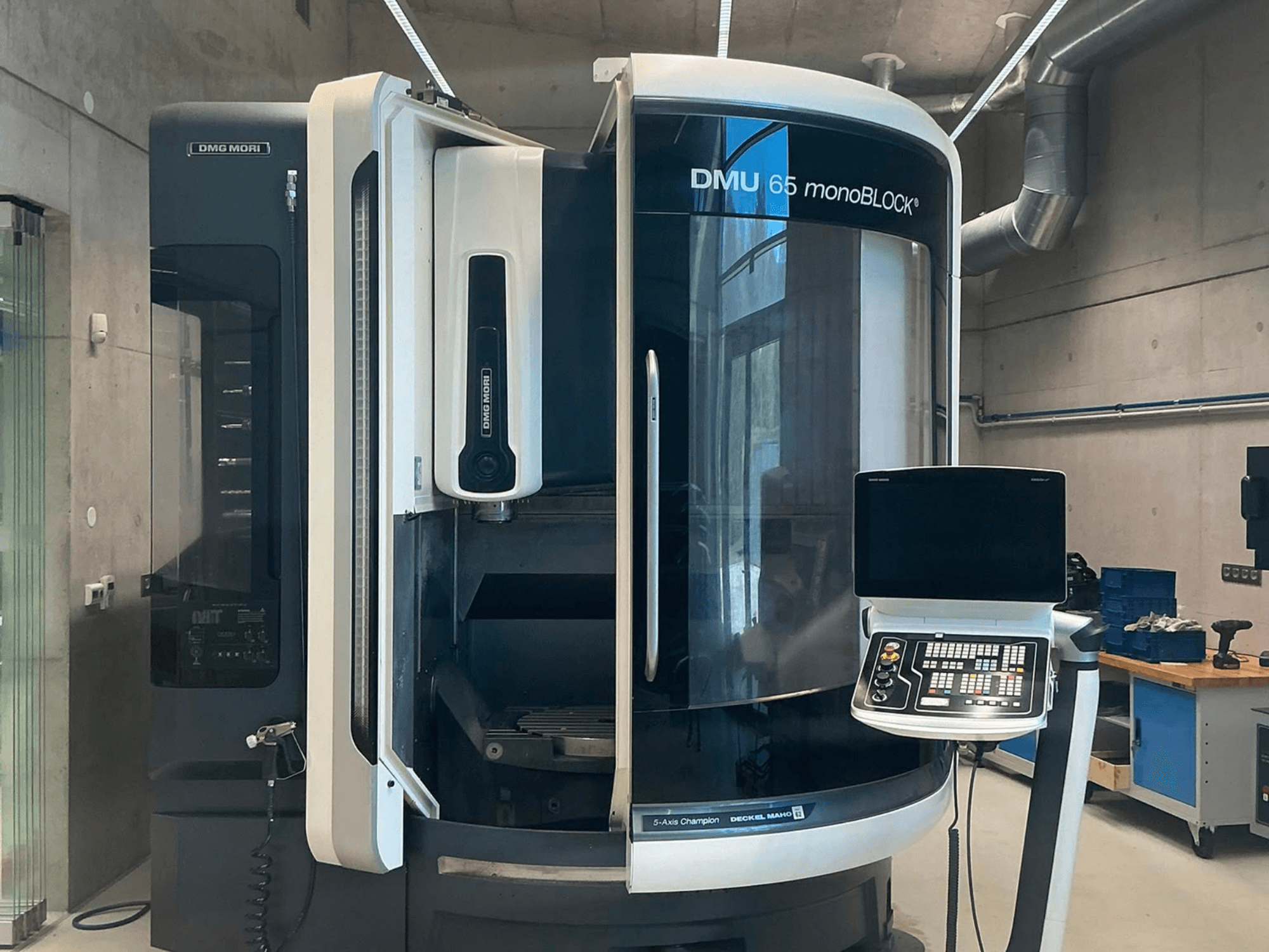 Centro de maquinagem vertical DMG MORI DMU 65 monoBLOCK, vista frontal, mostrando o painel de controlo e os detalhes da máquina num ambiente de oficina.