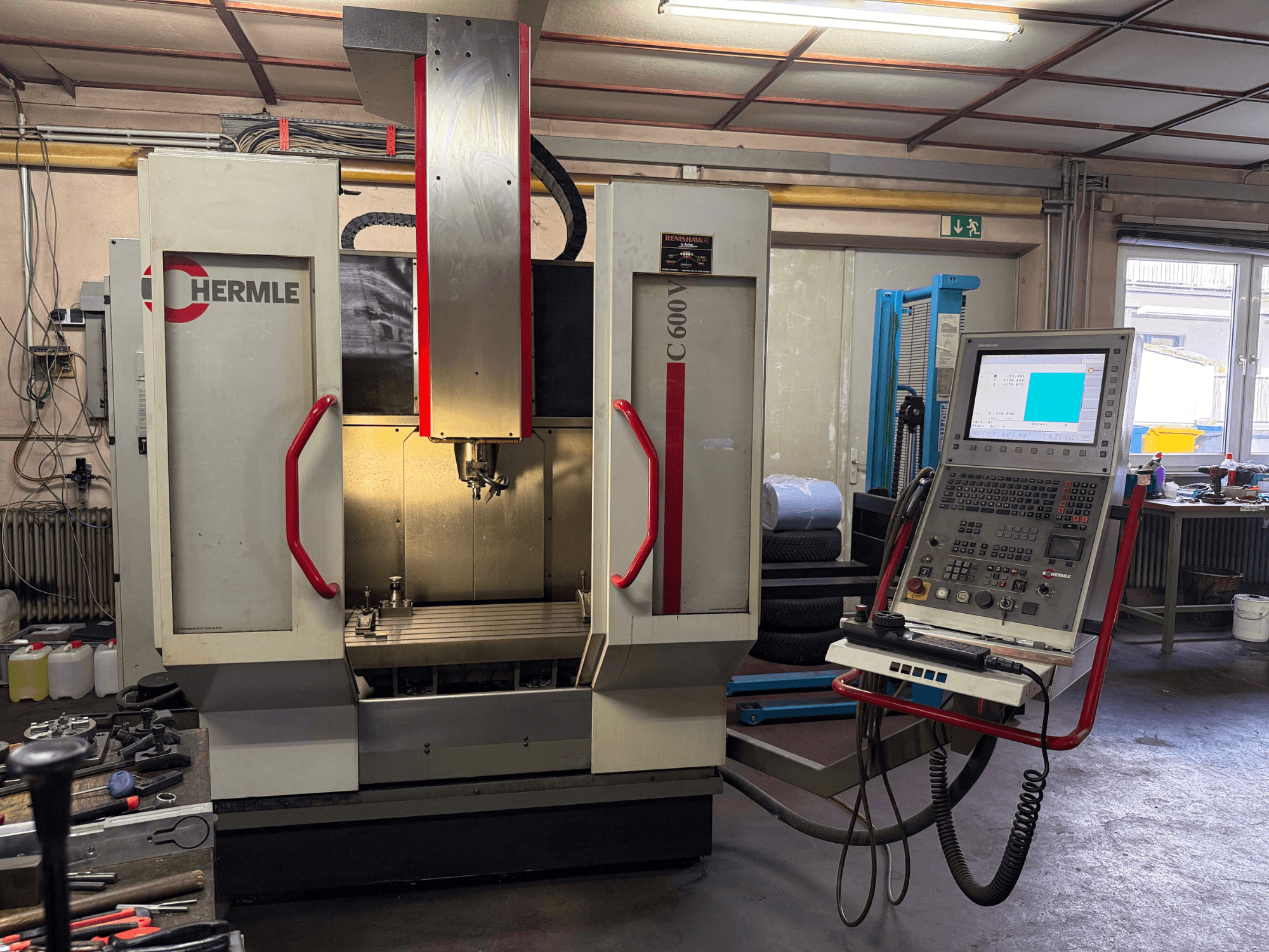 Fresadora CNC Hermle C 600 em vista frontal, com um painel de controlo com vários botões e uma área de trabalho espaçosa.