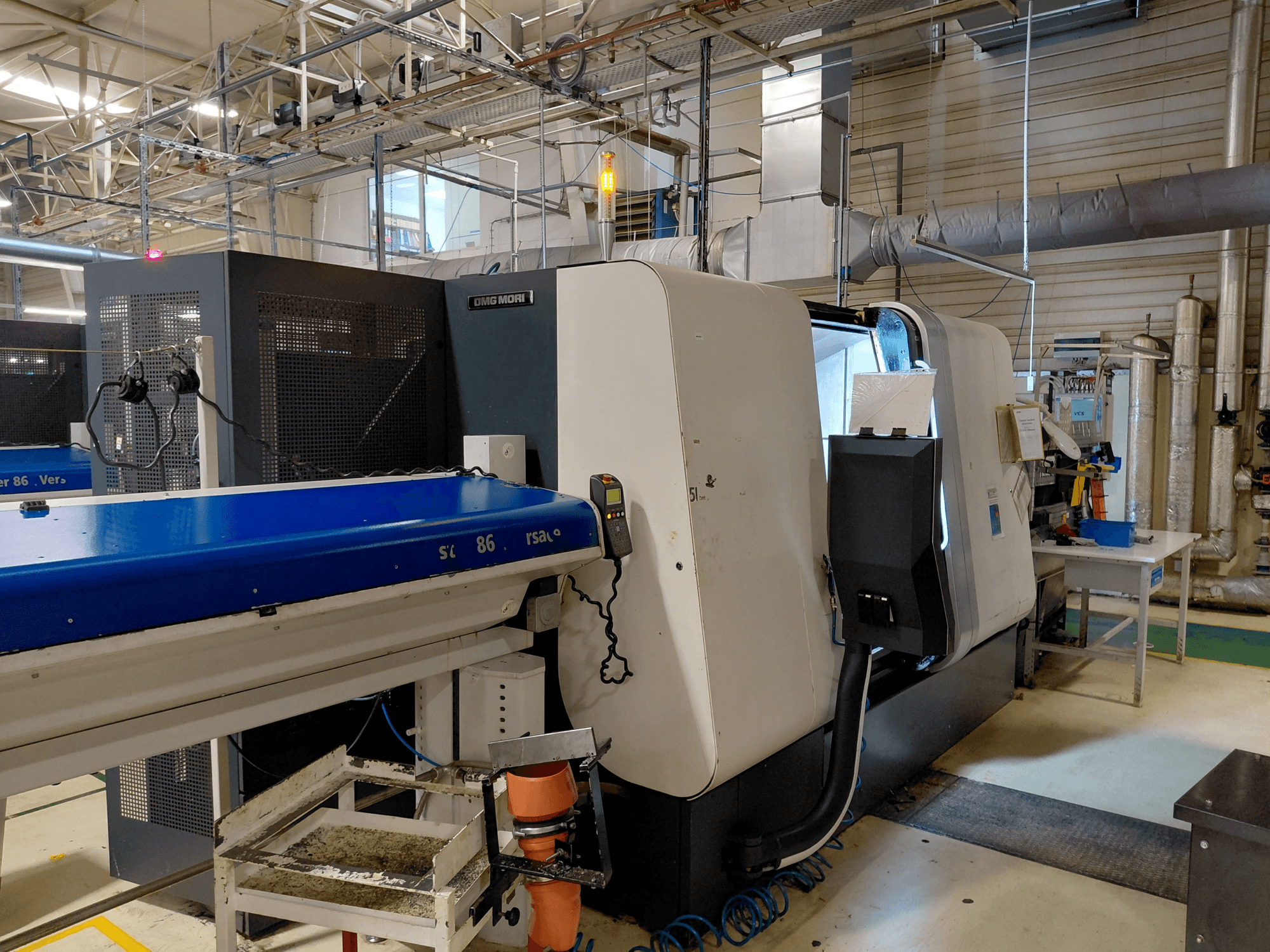 Torneiro multifuso linear DMG MORI Sprint 65, vista lateral com painel de comando e tapete rolante visíveis em oficina.
