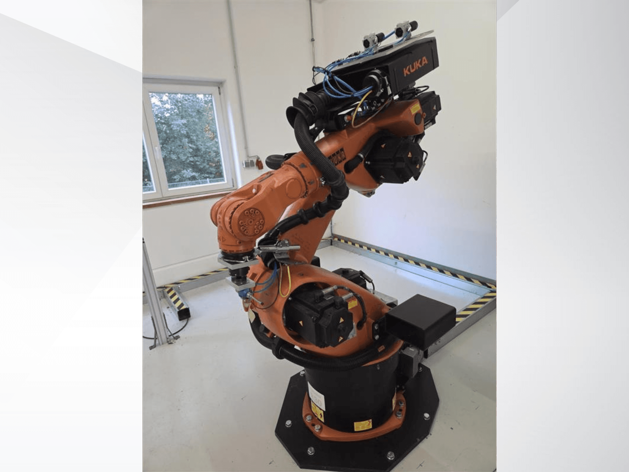 Braço robótico KUKA KR60 HA visto de lado, mostrando as articulações mecânicas e a cablagem numa base industrial.