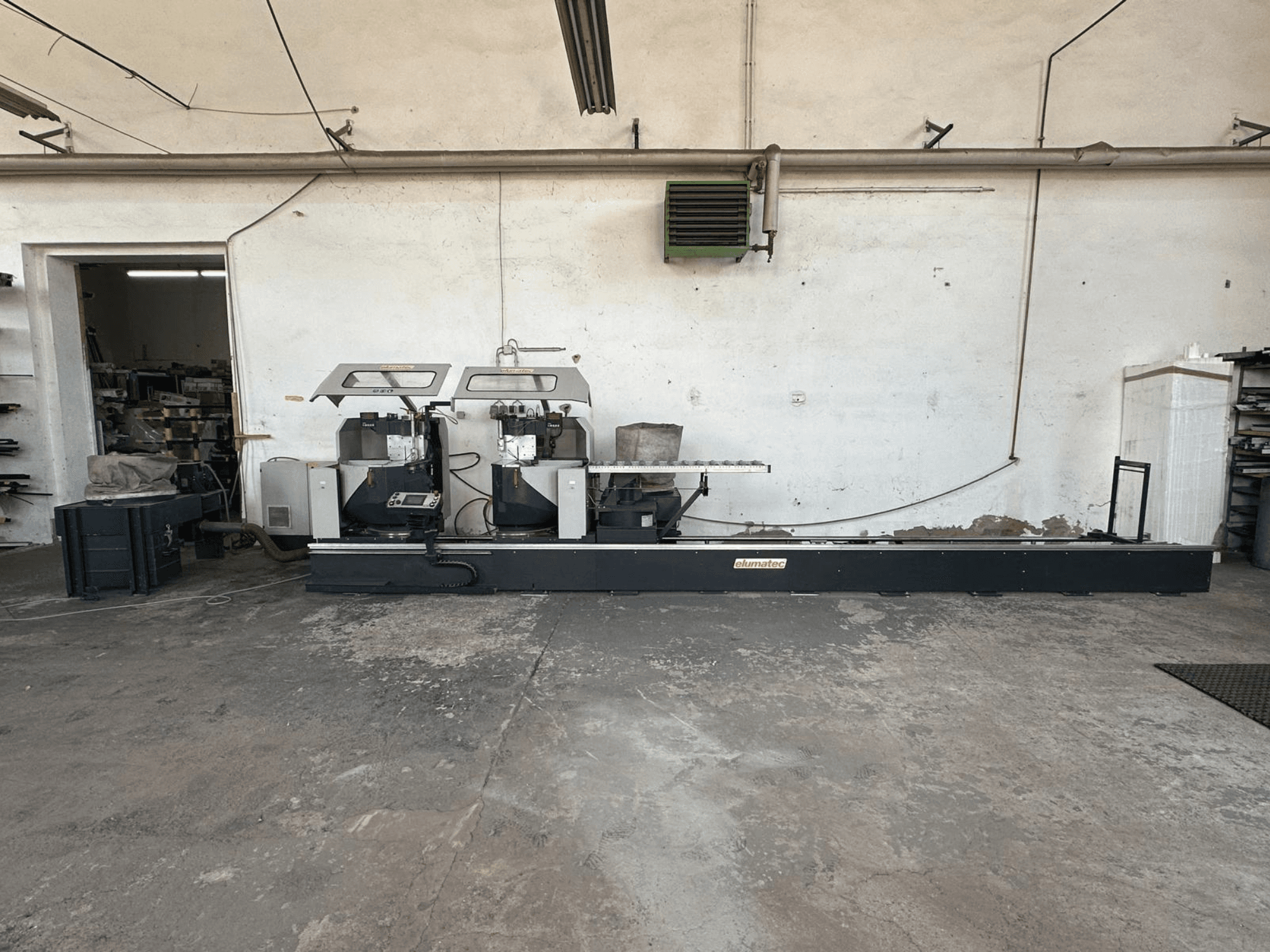 Serra circular para metal Elumatec DG 244 numa oficina, vista lateral mostrando serras duplas e controlos de funcionamento numa base robusta.